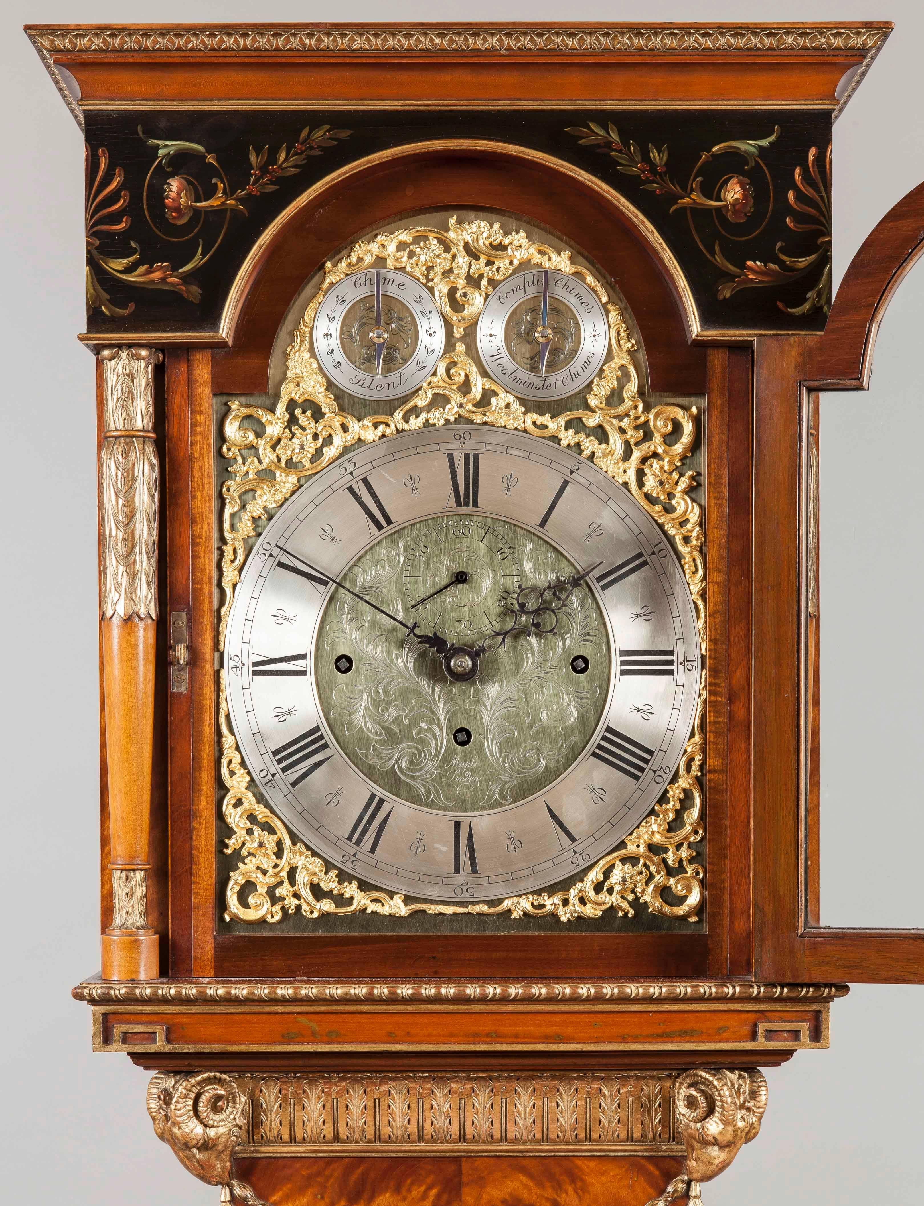 
A Long Case Clock by Maple and Company of London in the Adam Manner.

Constructed in a polychrome decorated satinwood, with extensive giltwood highlights; rising from swept bracket feet, the shaped inspection door having a central roundel of