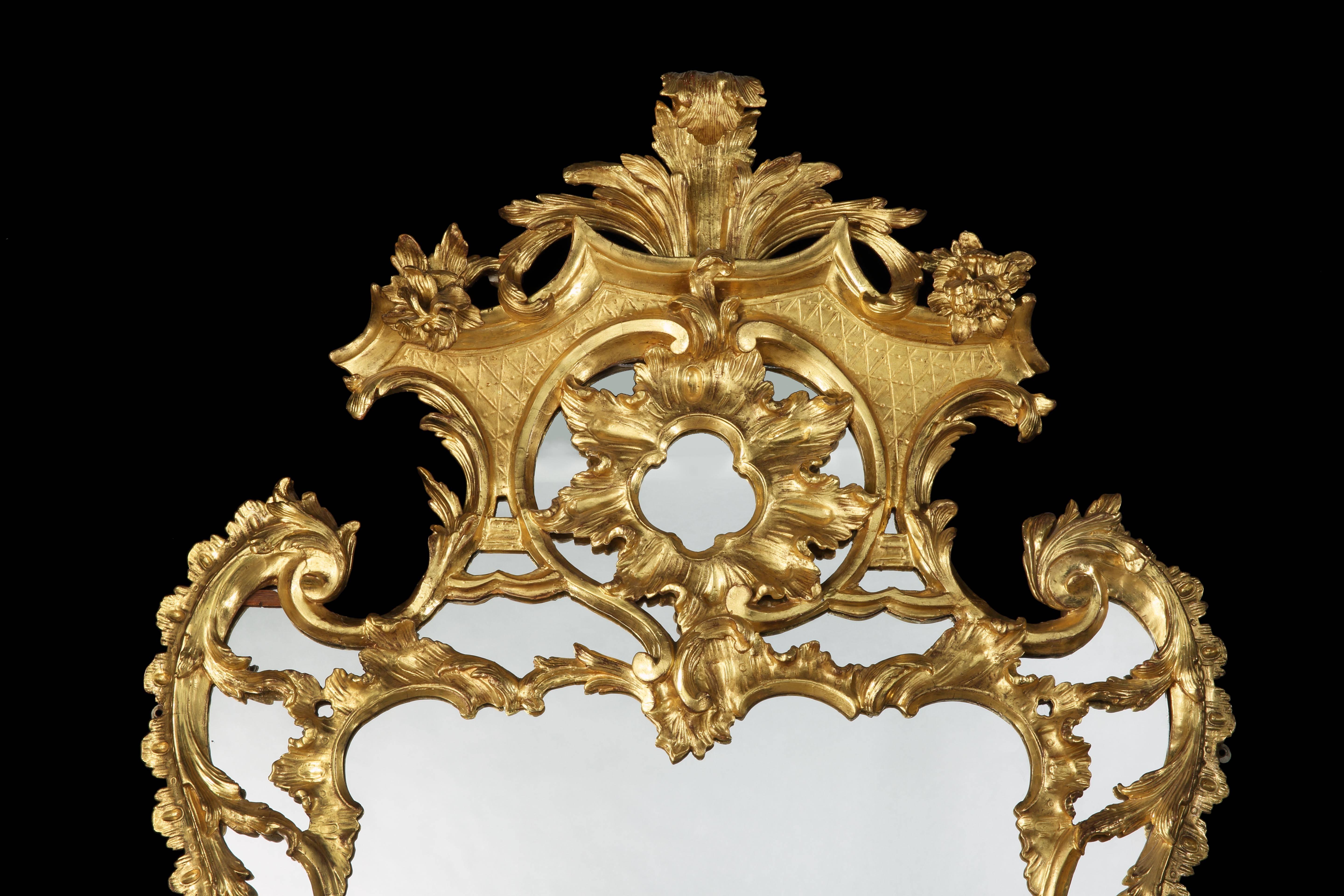 A giltwood mirror in the mid-18th century manner.

Enclosed within a carved and gilded swept and shaped symmetrical frame, adorned with ‘C’ scrolls, foliated and floral ornamentation, with a central divider separating the two large mirror plates,