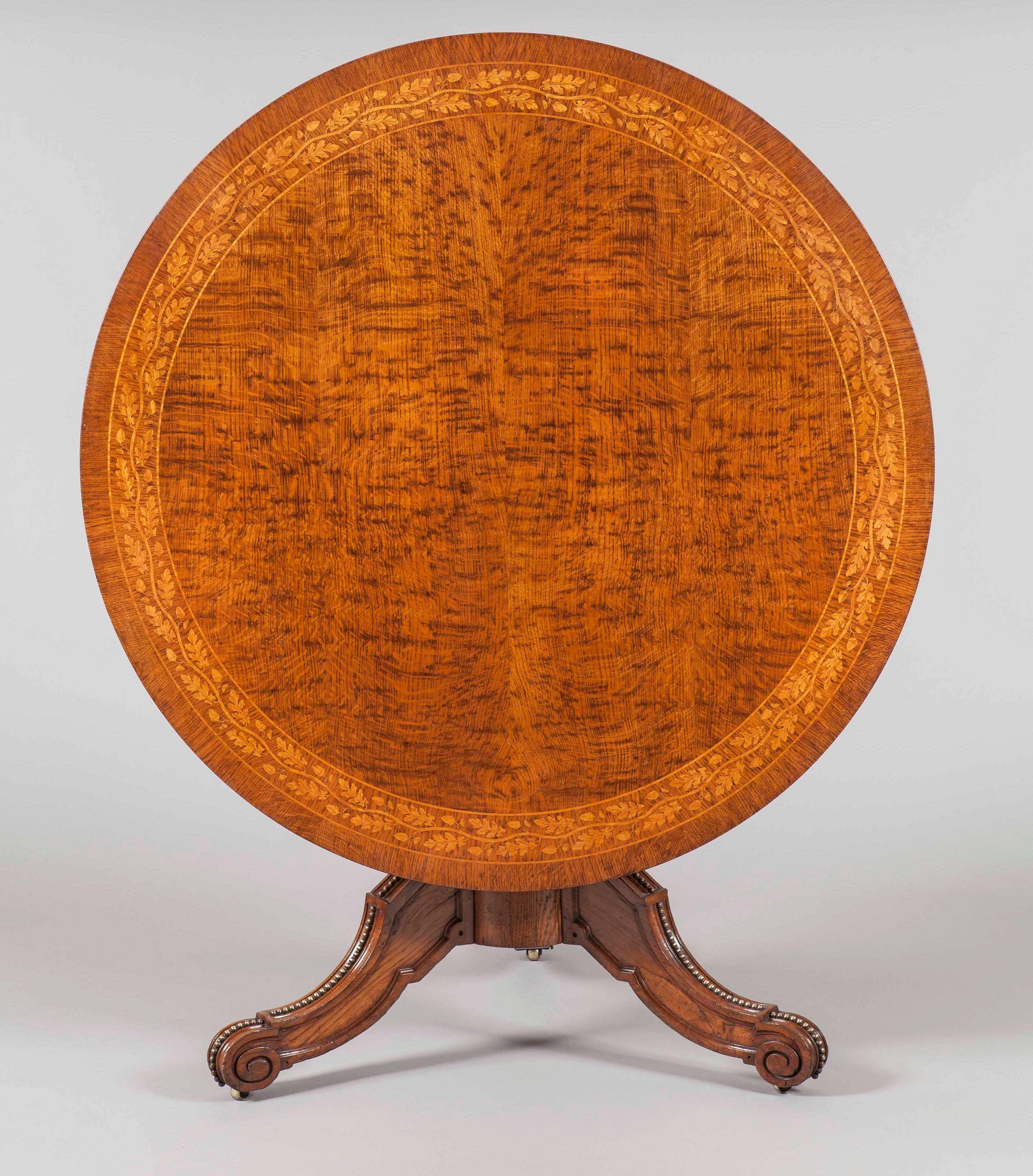 A fine inlaid Georgian center table.

Constructed in well figured oak, with maple inlay. The tripartite legs of stepped and hipped form, with scroll toes, with a trailing carved pearl motif. The central column turned, with a tilt top action, the