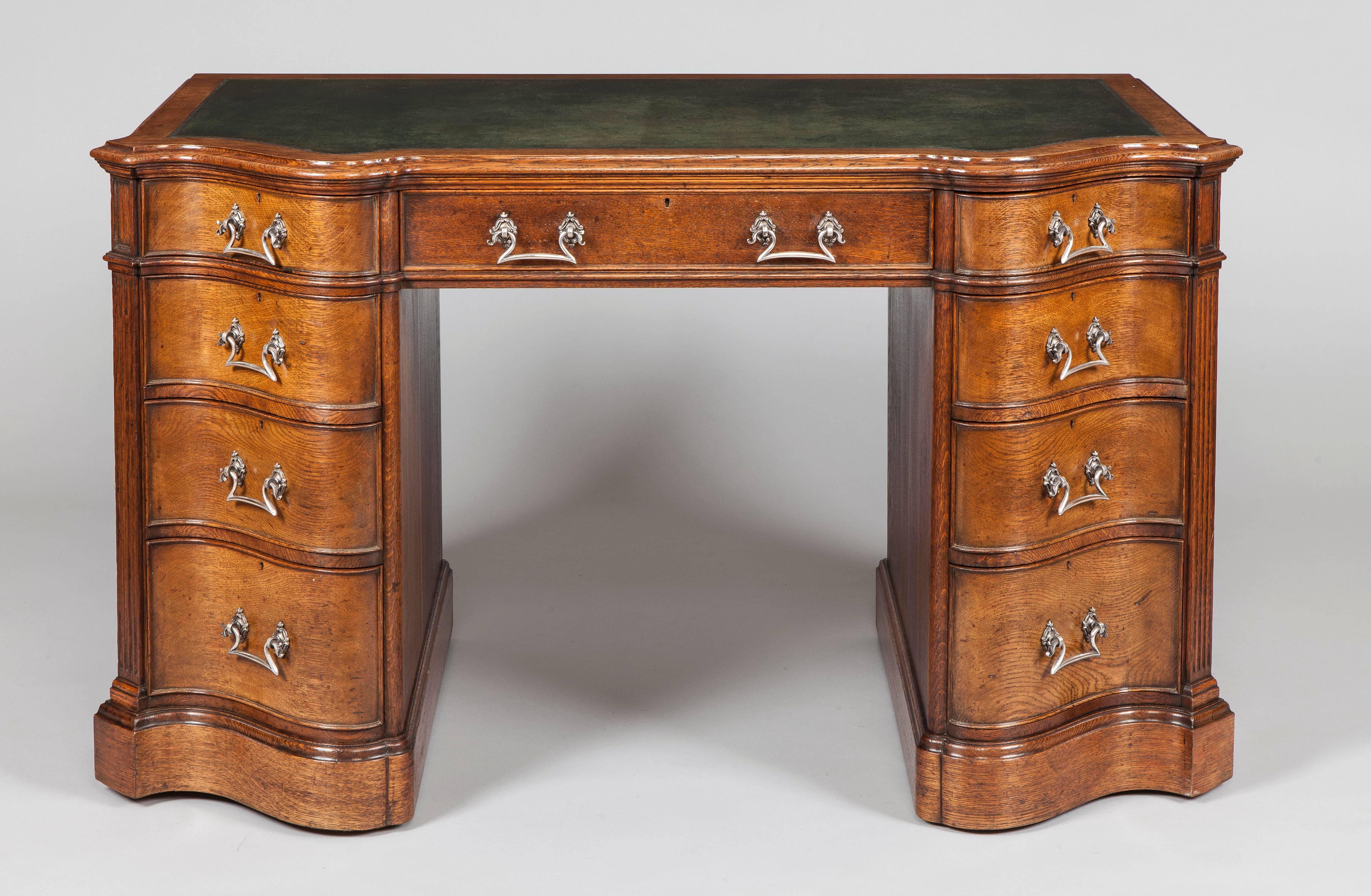 An Oak Pedestal Desk
After a design by Thomas Chippendale

Of freestanding serpentine form, rising from a plinth base, the pedestals each house four ‘S shaped’ front drawers with canted corners and carved fluted pilasters, a central drawer on top,