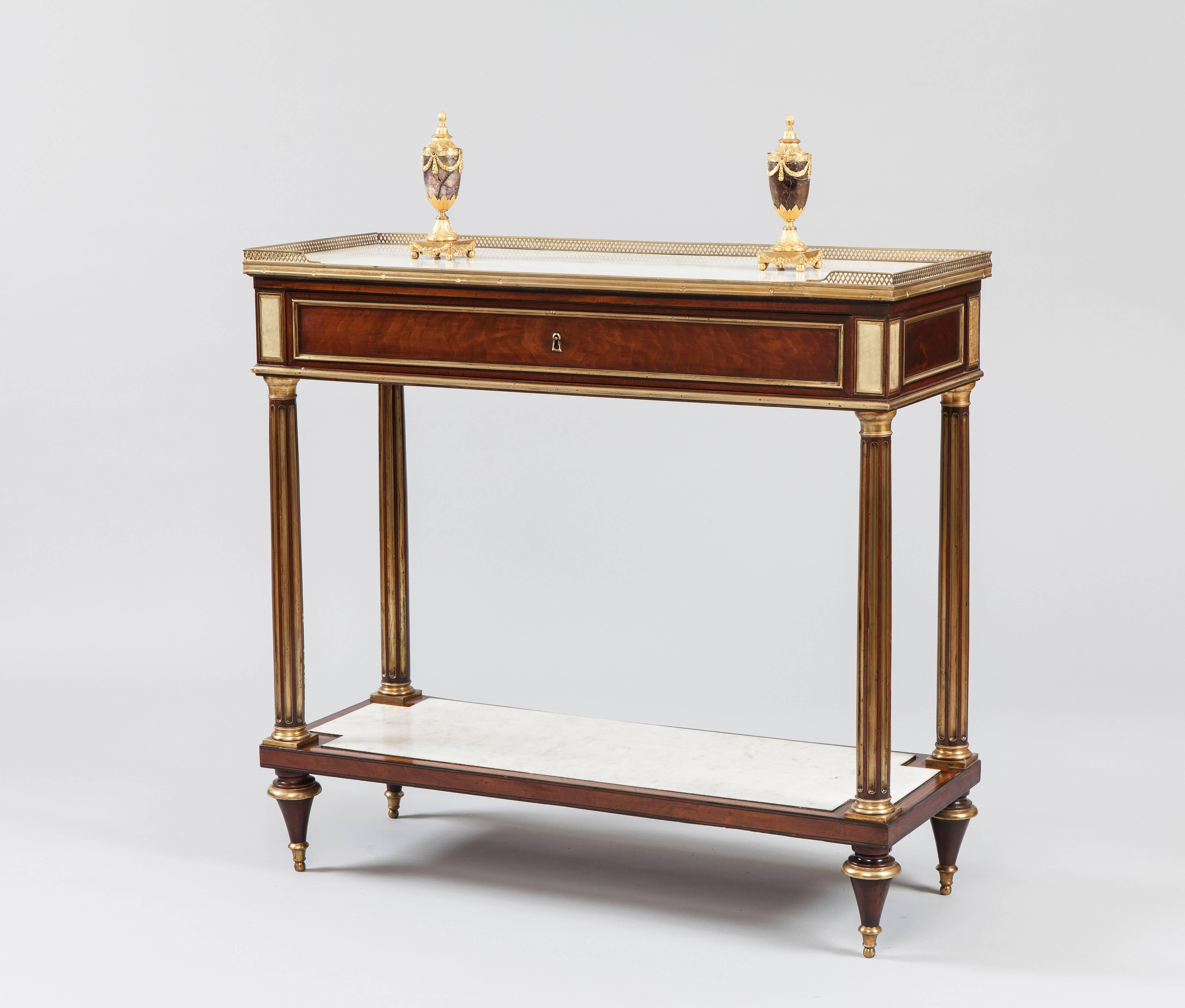 A good console-desserte of the Directoire period.

Constructed in mahogany, having ormolu and brass accents; rising from toupie feet, the lower tier having an inset shaped Carrara marble tablet, the four legs of entasis form with channelling with