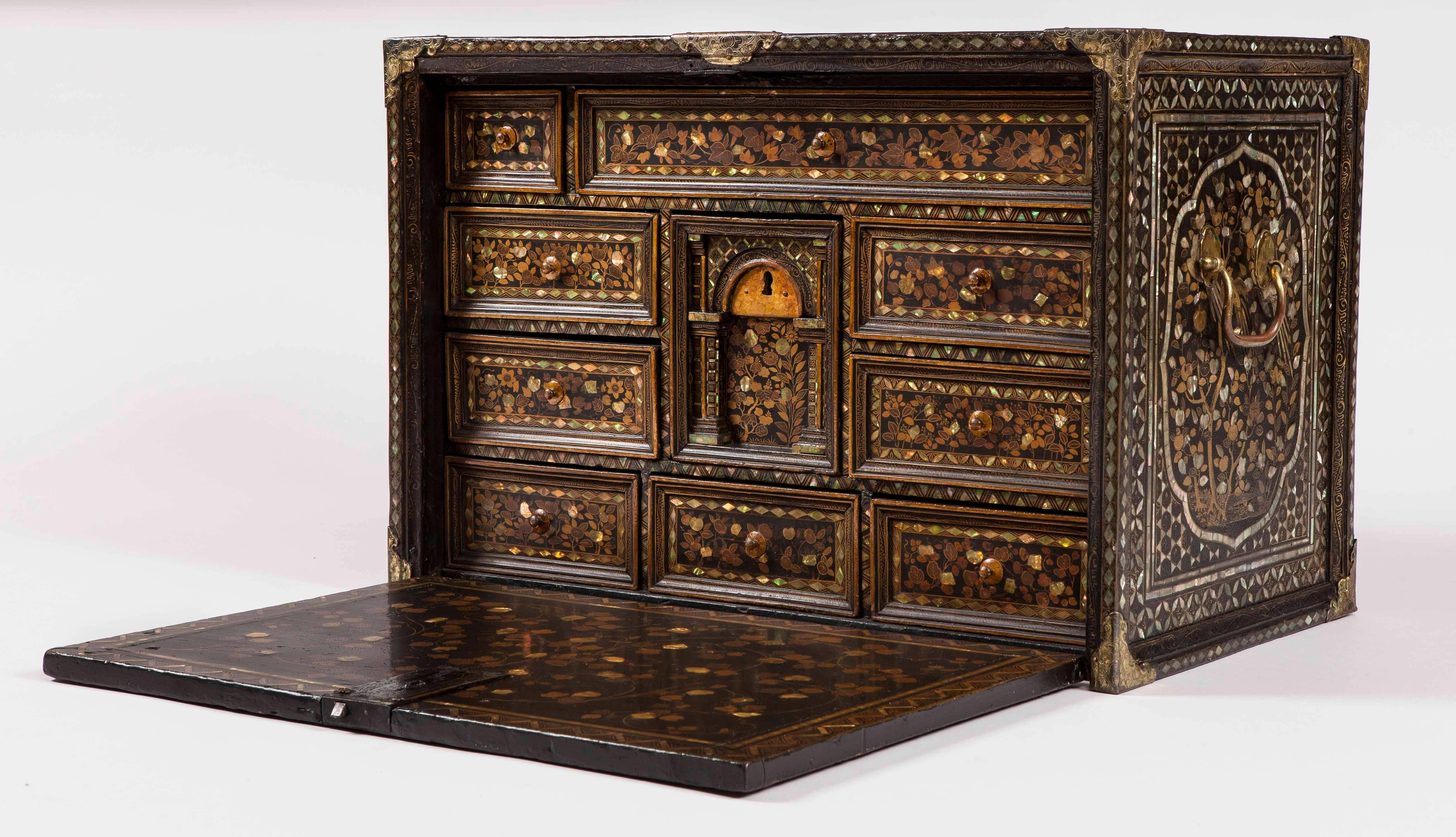 A 'Namban' export cabinet of the early 17th century

Of rectangular form, dressed with engraved metal guard straps at the angles, being comprehensively decorated with lacquer work, mother-of-pearl and gilt; having a hinged fall front, with an
