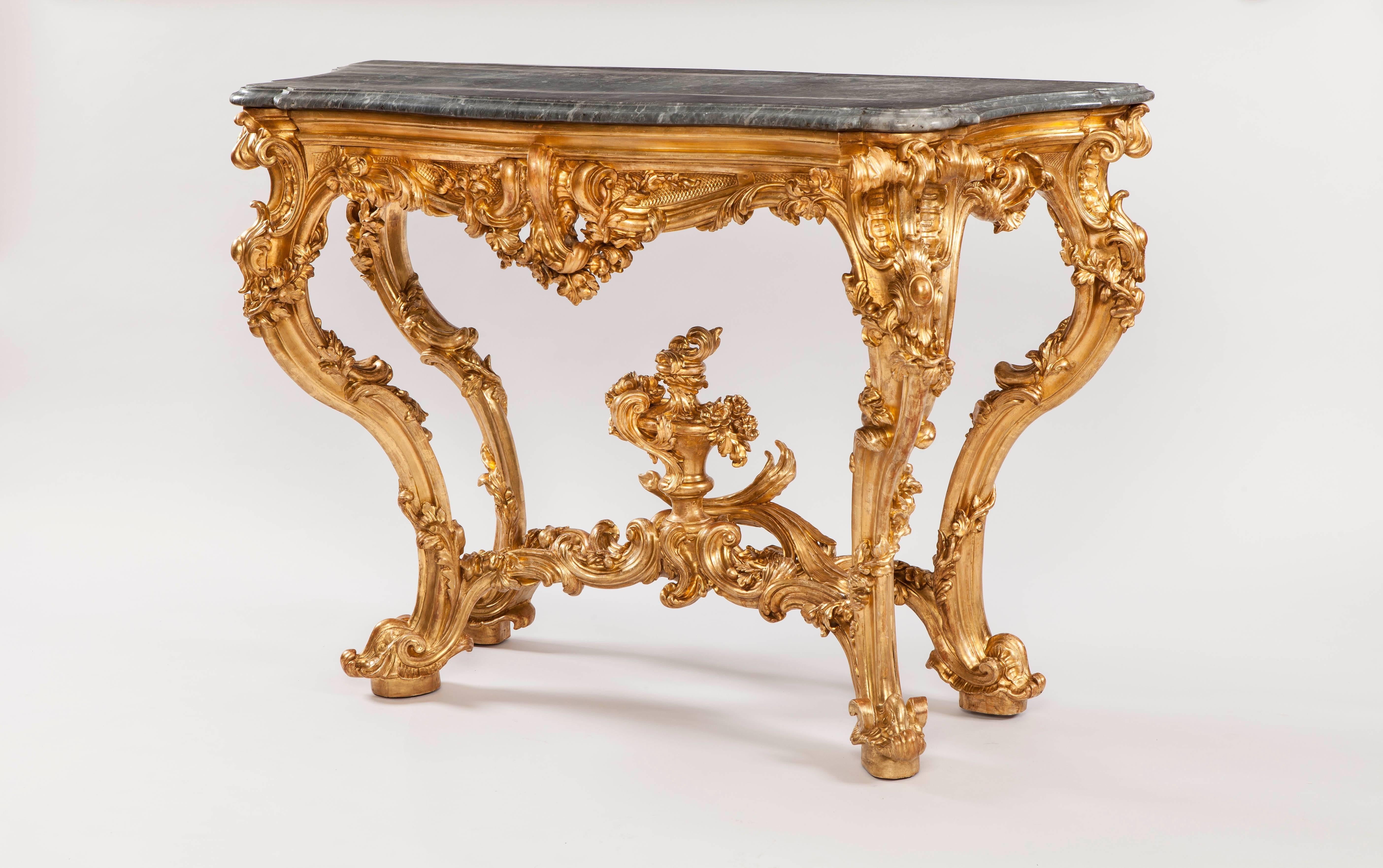 Constructed in carved giltwood, with shaped marble tops; each with four cabriole legs, ornately dressed with foliates are conjoined by shaped and floridly carved stretchers having stylised flambeaux finials at the centres; the shaped 'c' scroll