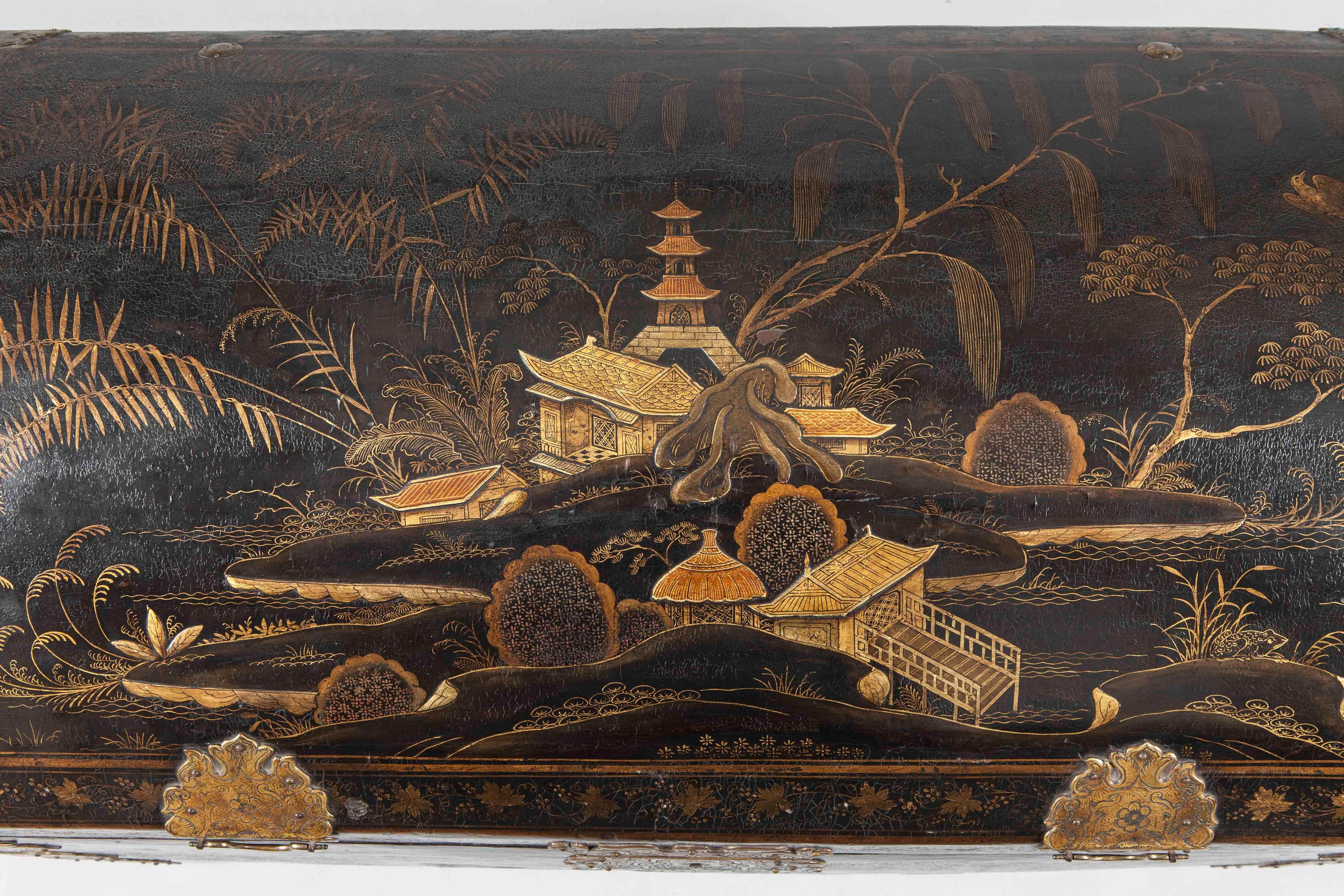 An early 18th century Chinese coffer on stand.

The coffer of domed form, lockable, and lacquered with bucolic Chinese landscape scenes in gilt and polychrome on a black ground; extensively fitted with brass strapwork and lockplates, engraved in