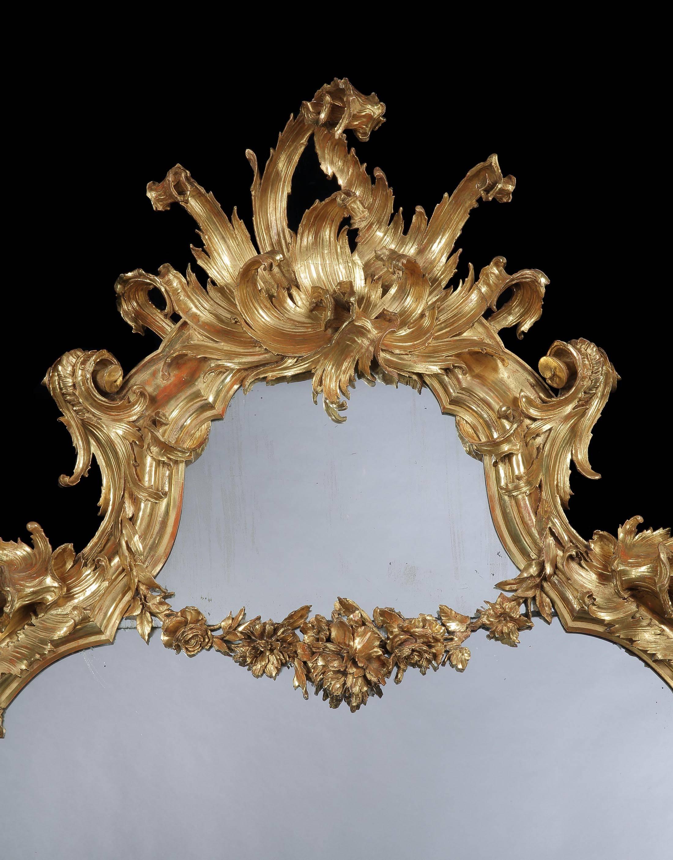 With an elaborately caved gold leaf framed with free scrolling lappet branches in the rococo style, the base with inverted cabriole legs and a central shell and leaf cartouche, the plate divided by a floral garland and the whole surmounted by an