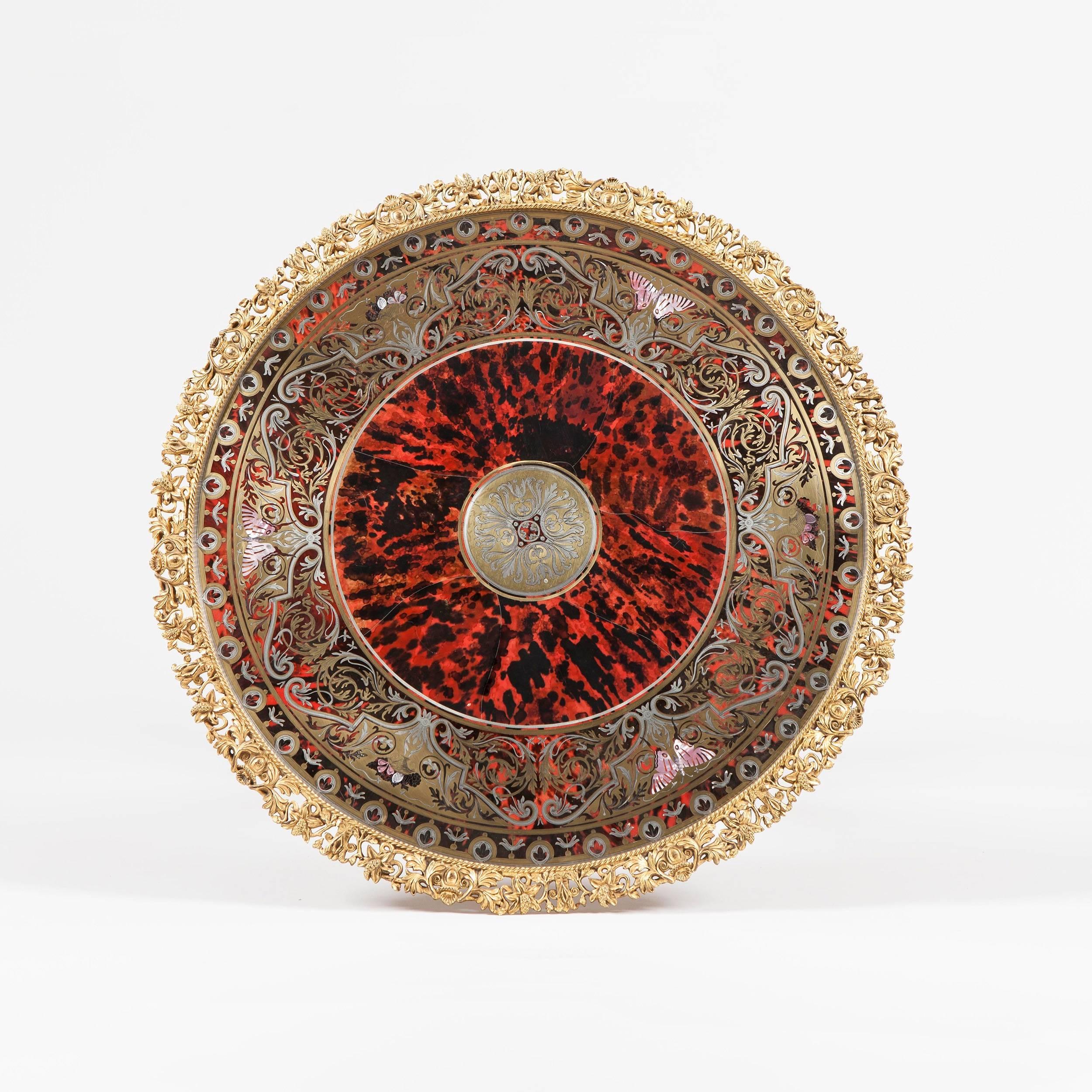 The whole of red tortoiseshell inlaid with silver pewter and gold brass marquetry or premier-parte mounted with finely cast gold gilt bronze mounts, the circular top decorated with designs of arabesques, foliage and butterflies of mother-of-pearl,