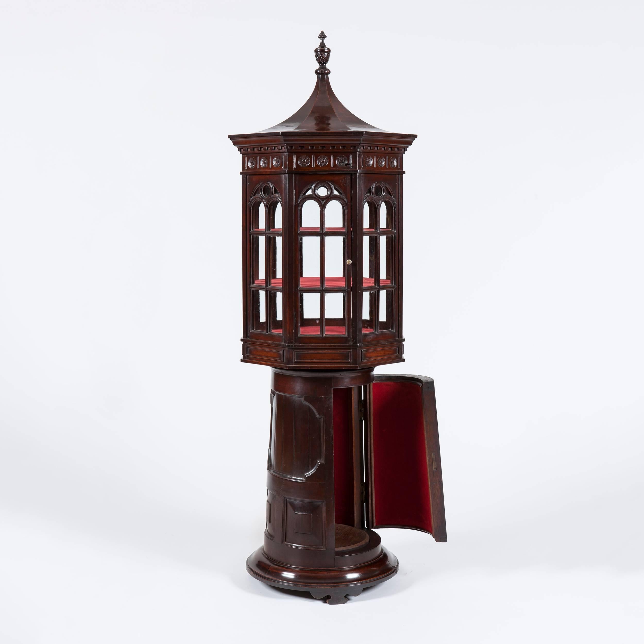 An Unusual Display Cabinet of 'Lighthouse' form

Constructed in teak; rising from a circular plinth base, inset with a single lockable door housing a shelved interior; the rotating baize shelved top of octagonal form, housing Gothik lancet dressed