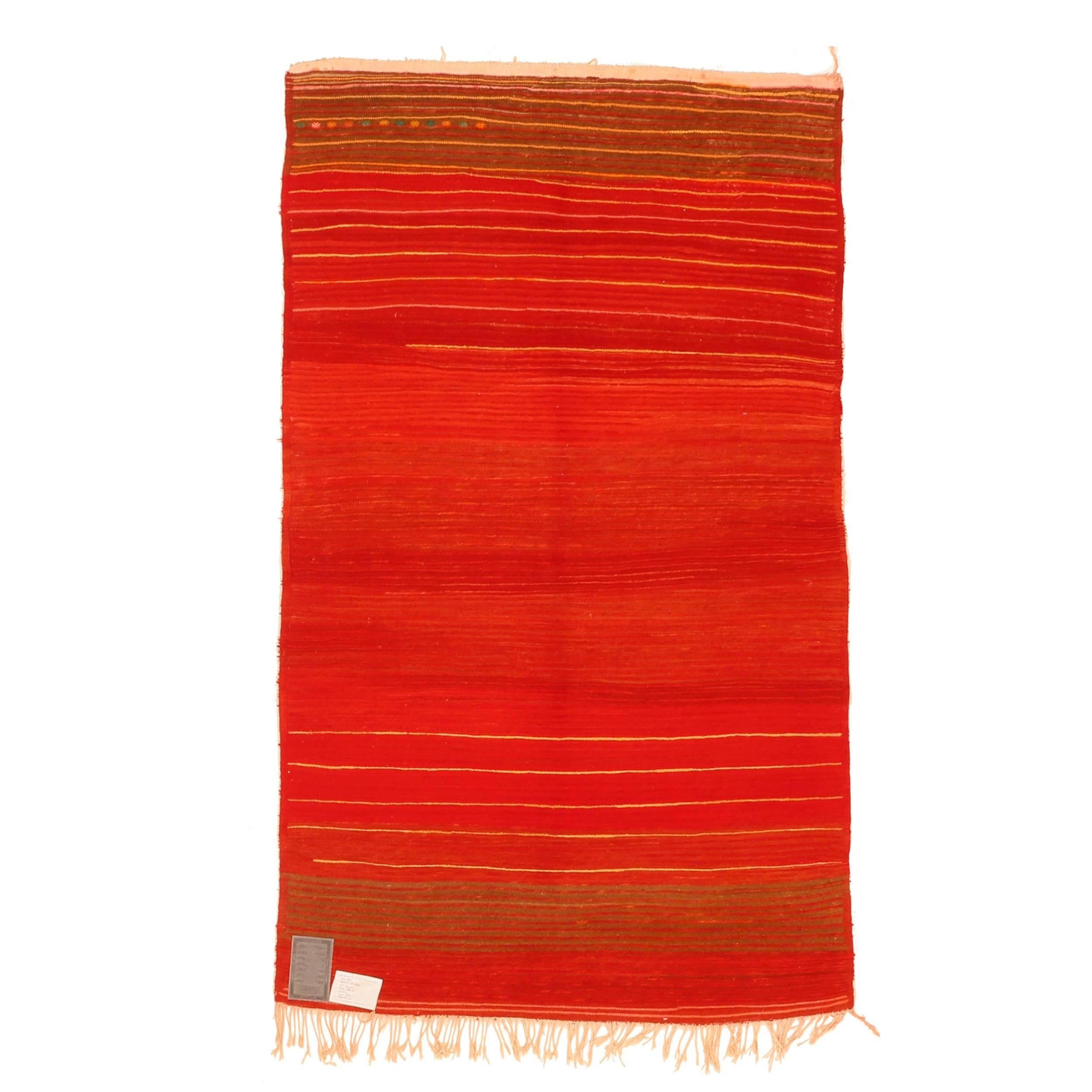 A rather unusual Berber rug from the Ait Sgogou tribe, located in the Moroccan Middle Atlas, distinguished by a rich red open field embellished at both ends by contorting horizontal lines in the shades of yellow, orange and rose. The end skirts are