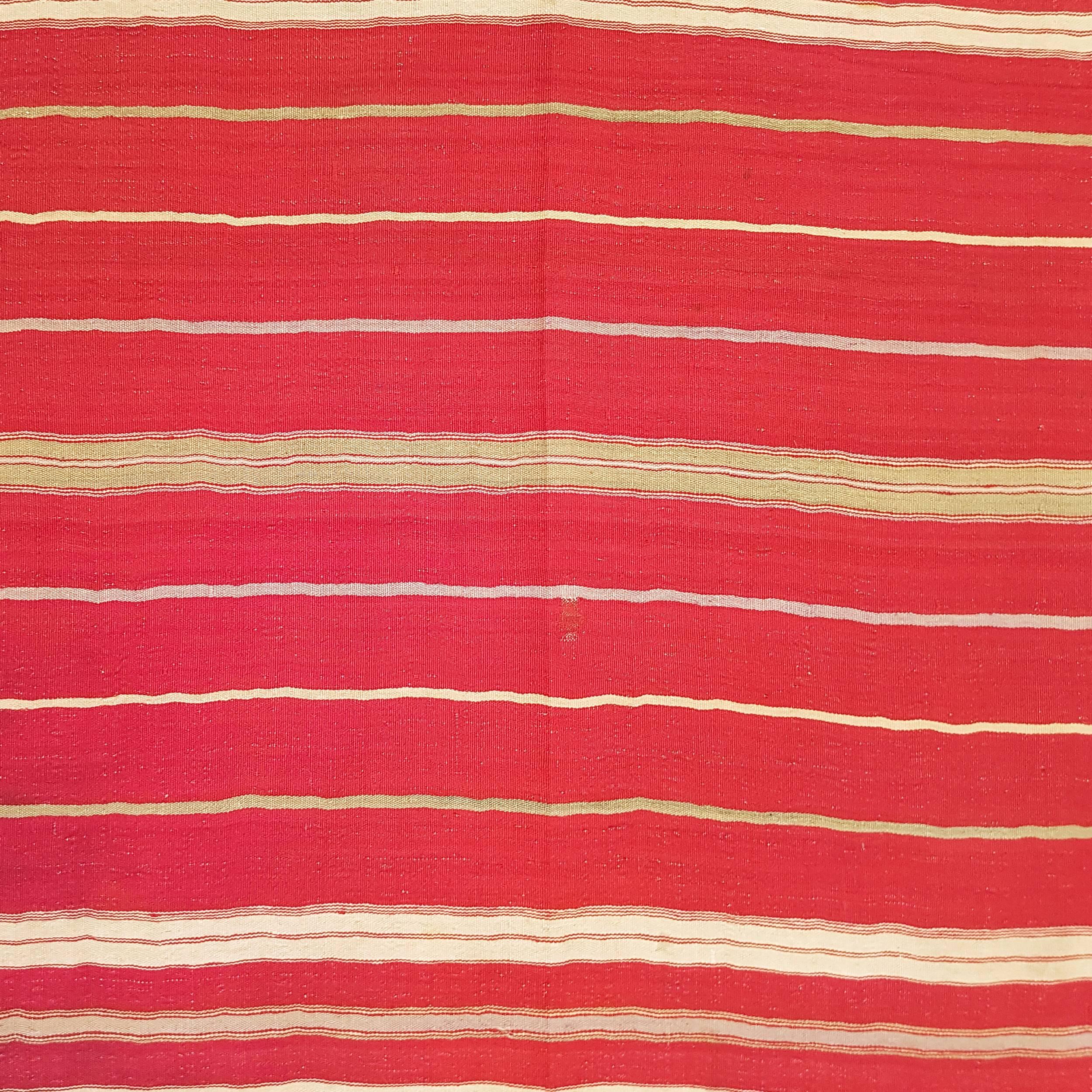 A very rare and unusual flat-weave, extremely finely woven with silky wool, decorated by an asymmetrical array of horizontal stripes on a rich red background, save for the lower third of the field which is in ivory.
A textile imbued with a strong