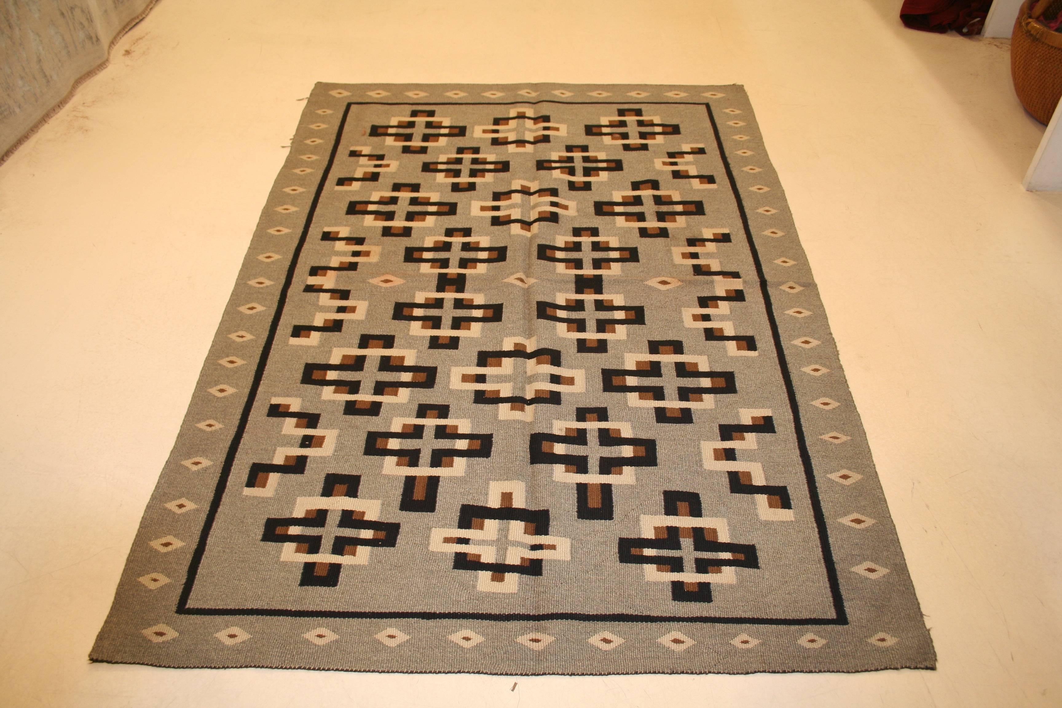 Ein antiker Navajo-Teppich aus dem Südwesten Amerikas, der sich durch ein Allover-Muster aus kreuzförmigen Elementen auf einem weichen grauen Hintergrund auszeichnet. Diese Teppiche werden wegen ihres authentischen volkstümlichen Charakters