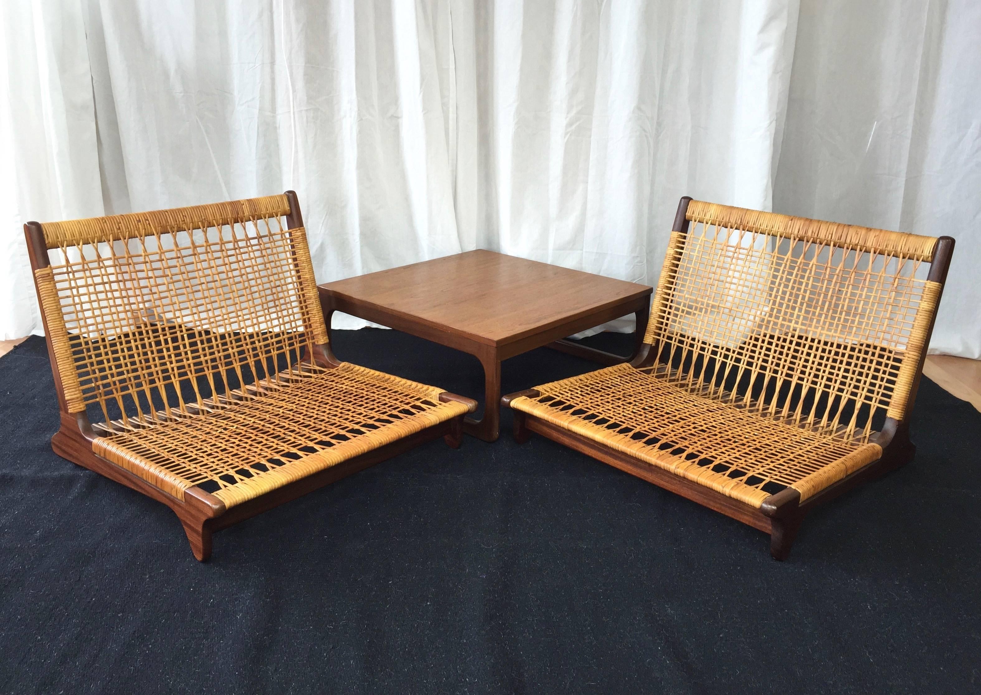 A scene-stealing low lounge chair and table set designed by Hans Olsen for Brahmin.

Pair of stained teak frame ultra-low loungers feature woven cane seats in great original condition. Accompanied by a matching top low side table with stained teak