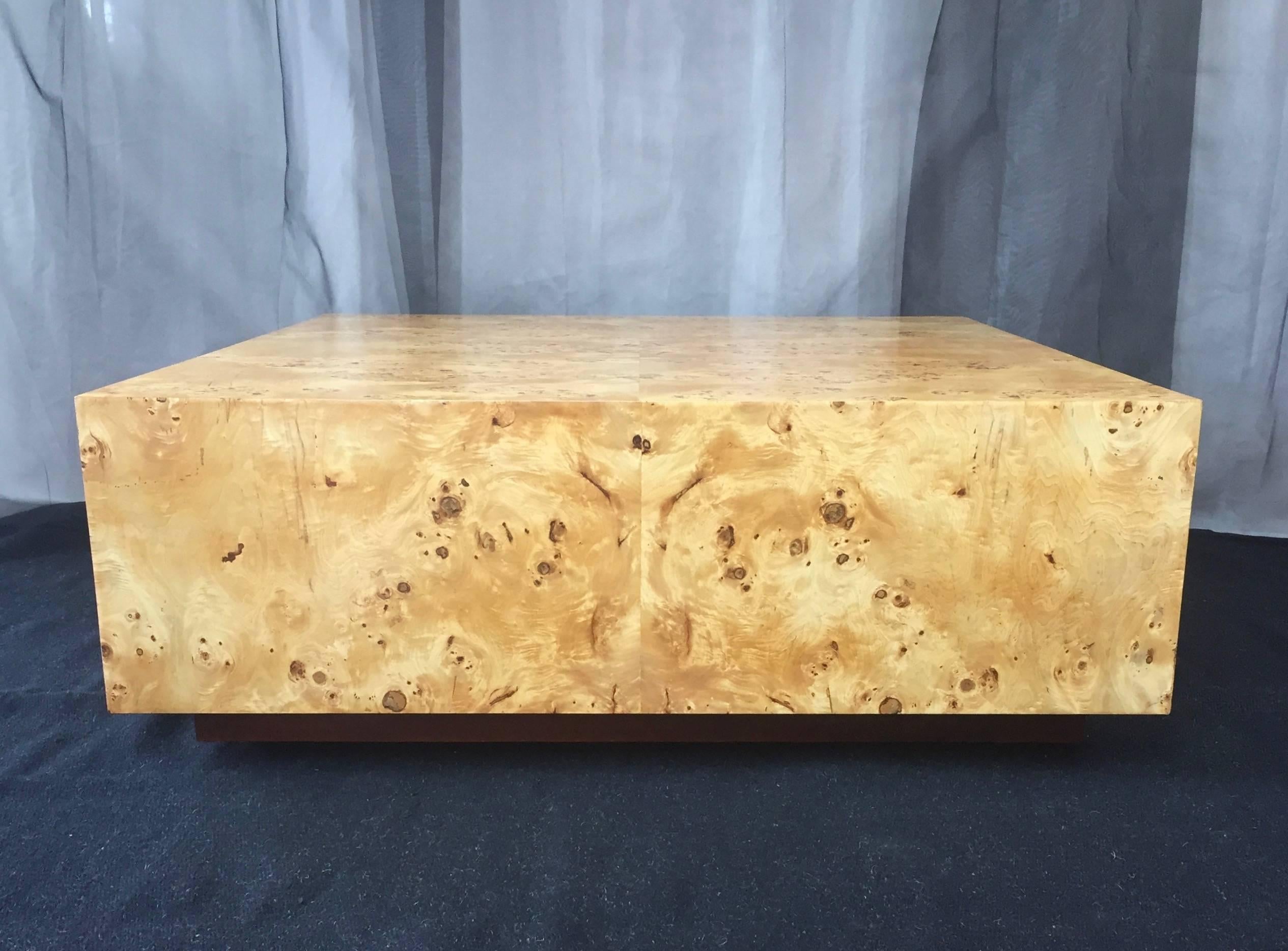 A very substantial square coffee table finished in burl wood and attributed to Milo Baughman.

Simple form showcases shimmering bookmatched Carpathian elm burl veneer. Its exceptionally lively figure evokes a dazzling desert landscape viewed from