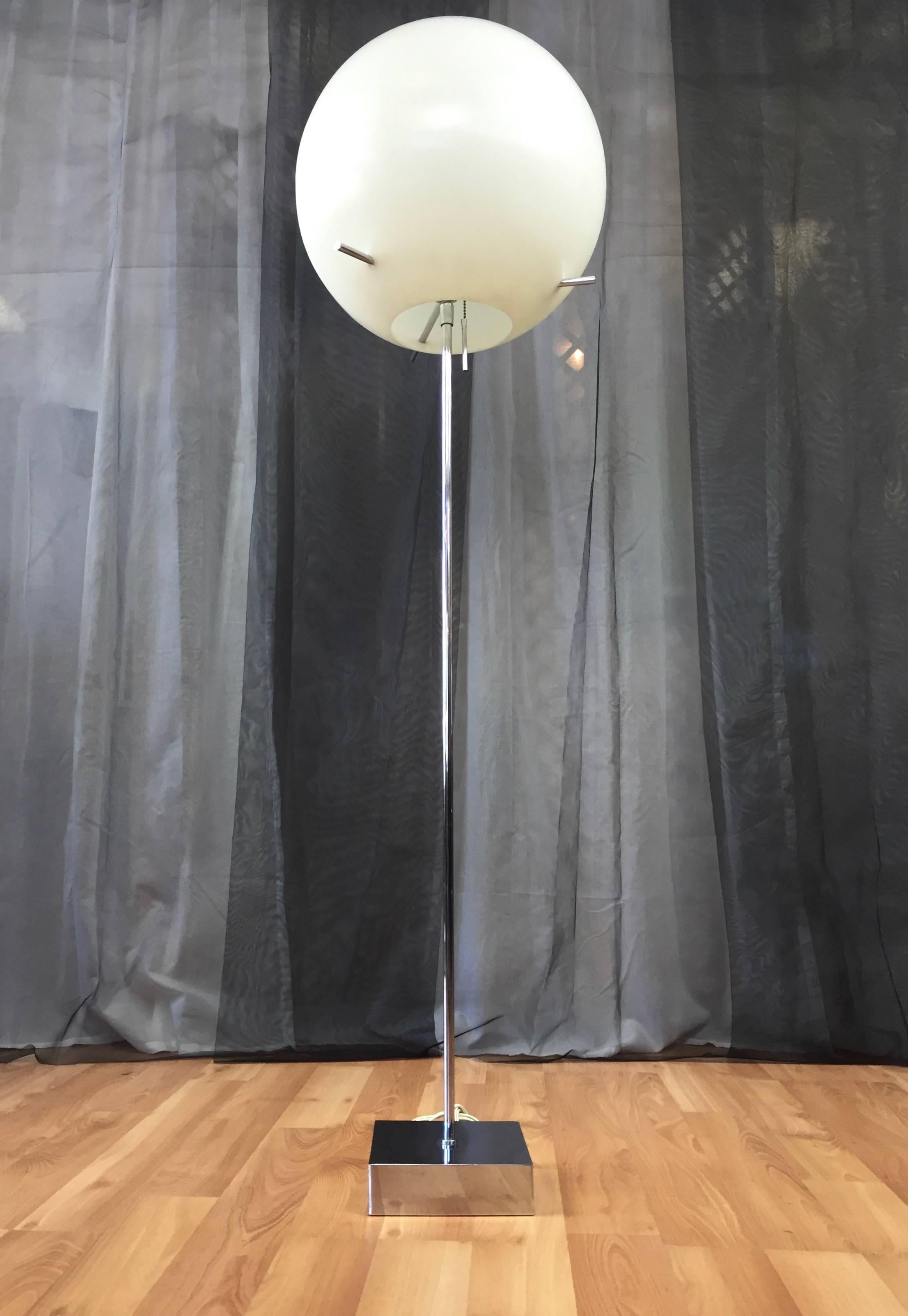 An ultra-modern chrome floor lamp with white globe shade by Paul Mayen for Habitat.

Minimalist mirror-finish base and stem support an oversized balloon like plastic globe shade. A trio of chrome rods pierce the shade’s side, and serve as handles