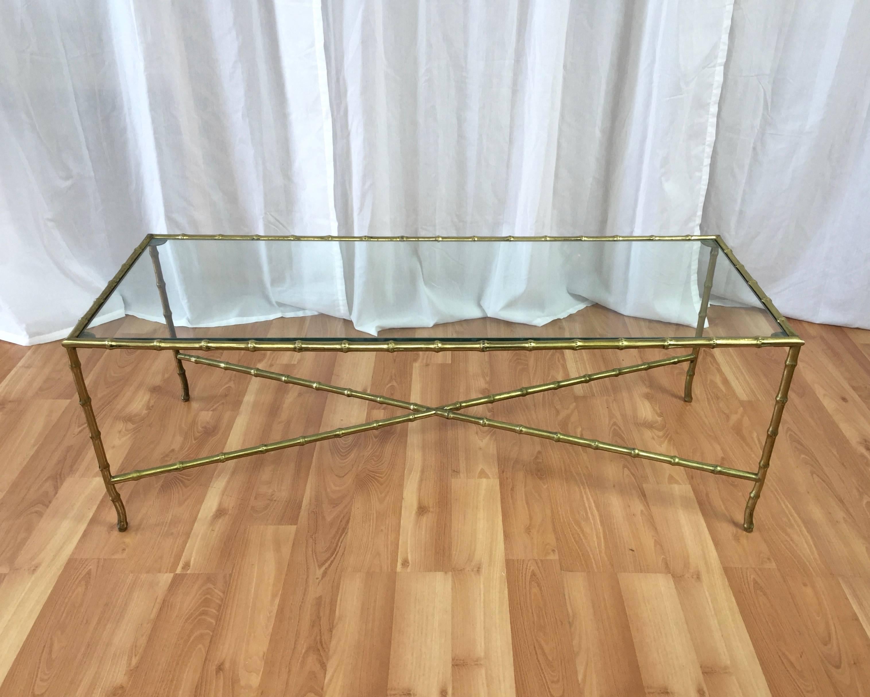 A Hollywood Regency or chinoiserie style brass and glass faux bamboo coffee table by Maison Baguès.

Very well rendered and visually light frame features elegantly curved ankles, and is grounded by an X-shaped stretcher. Brass finish is nicely