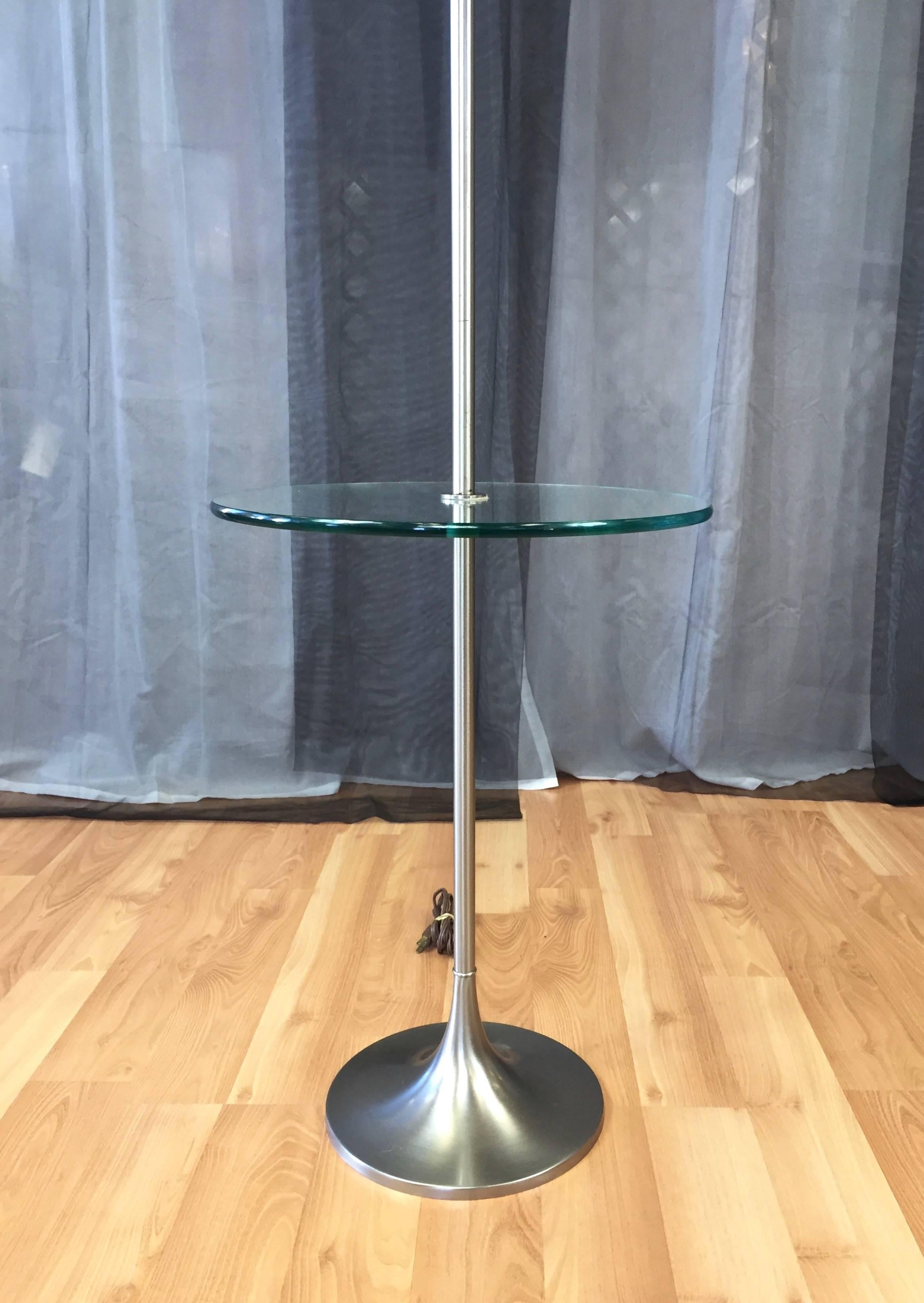 A Mid-Century Modern tulip base metal floor lamp with integrated glass table by the Laurel Lamp Manufacturing Company.

Satin finish brushed metal base and pole have a warm silver tone. 3/8-thick tempered glass table is suspended through its