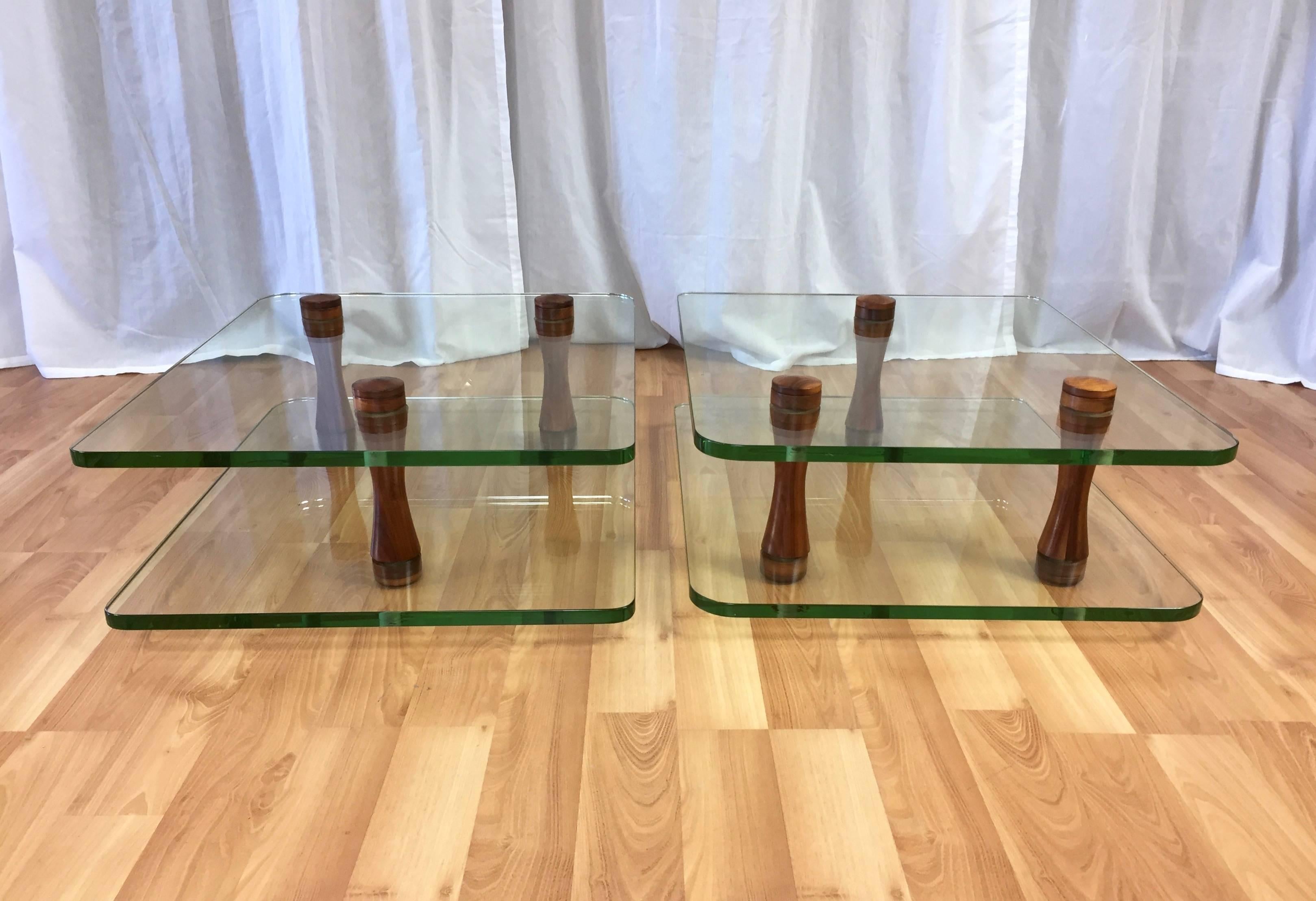 A rare pair of low two-tier glass and walnut end tables or occasional tables designed by Gilbert Rohde for Herman Miller.

Simple yet visually striking Mid-Century Modern design features a trio of solid walnut spindles that intersect and support