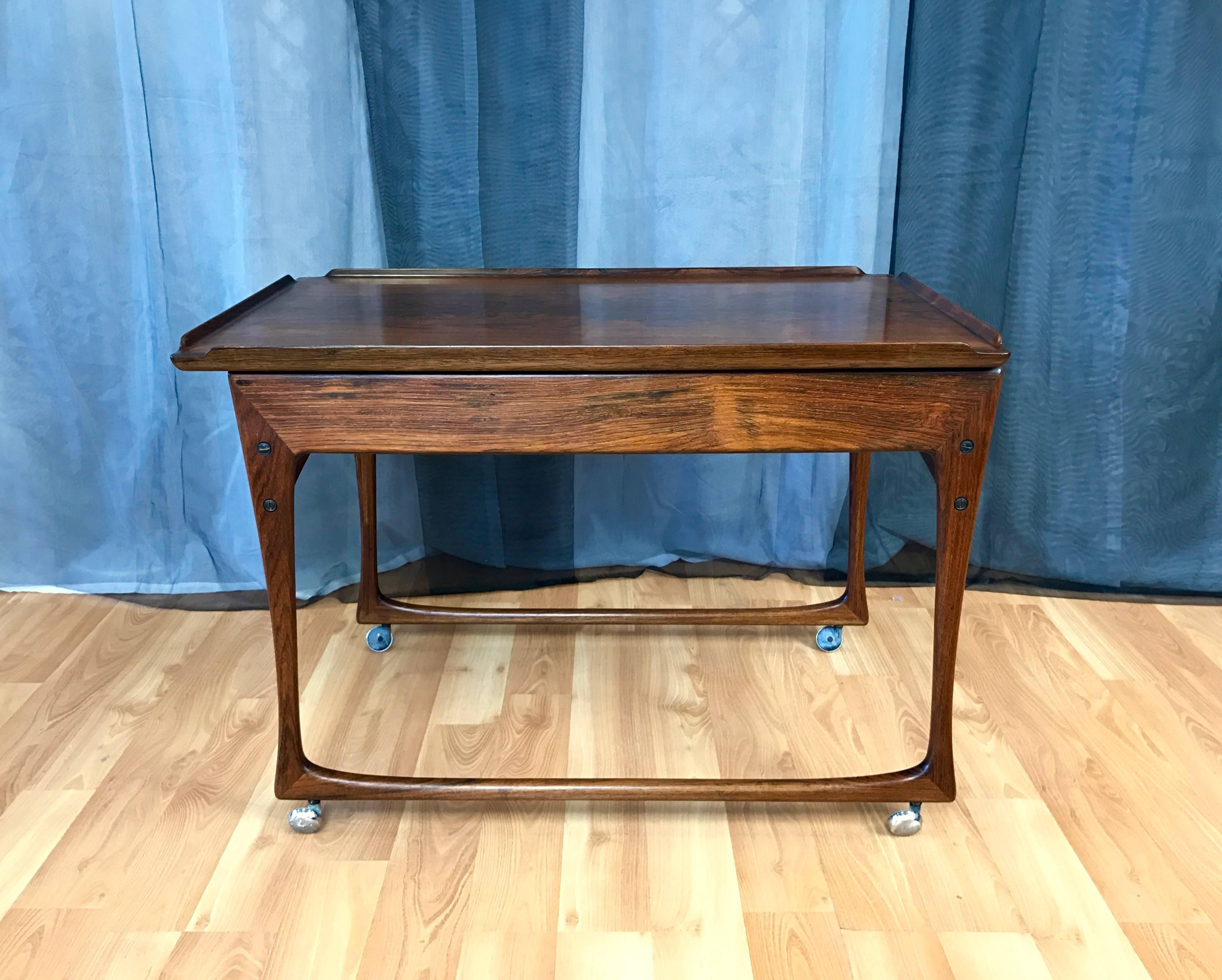An uncommon rosewood bar cart with sliding top by Denmark-based designer J. Ingvard Jensen, made in Odense, Denmark. Sculptural solid rosewood frame supports a bookmatched rosewood veneer top with solid rosewood lips. Top slides open to reveal a
