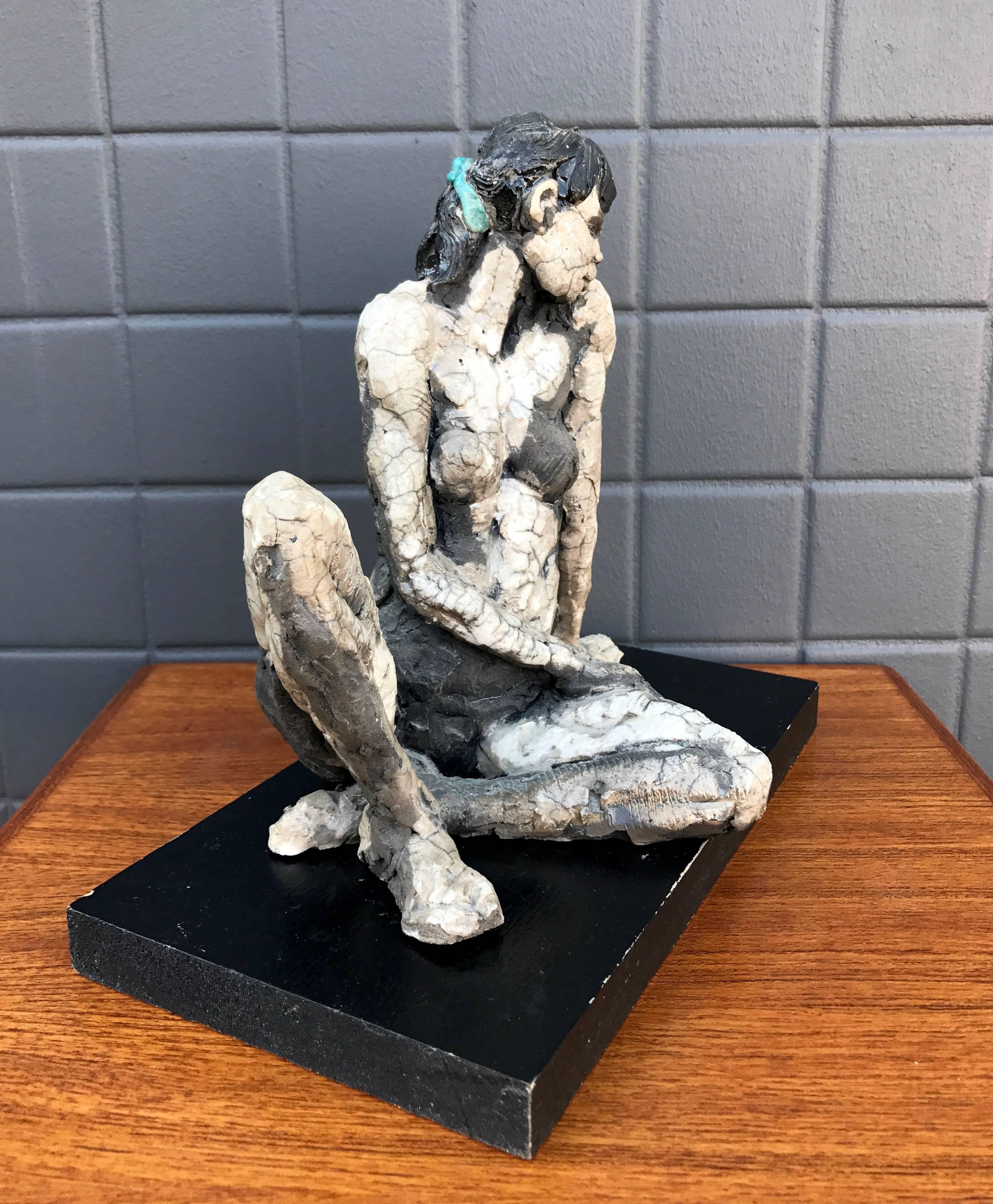 A raku fired ceramic sculpture of a reclining woman on original pedestal by California Bay Area artist Lana Federico.

Loosely sculpted piece features traditional glaze on hair and ribbon, with Japanese-style raku craquelure glaze contrasting with