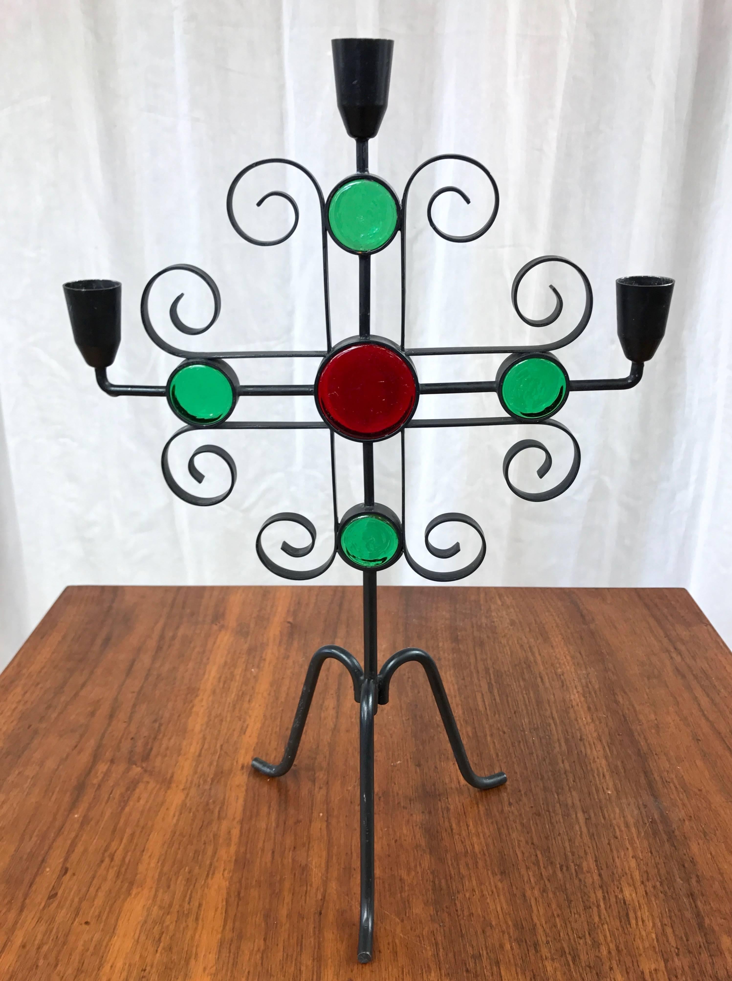 A tall wrought iron candelabra-style candleholder with glass accents by Gunnar Ander for Ystad-Metall.

Its curlicues and vibrant colors represent a delightful Mid-Century Modern interpretation of traditional Swedish design motifs. Finished in