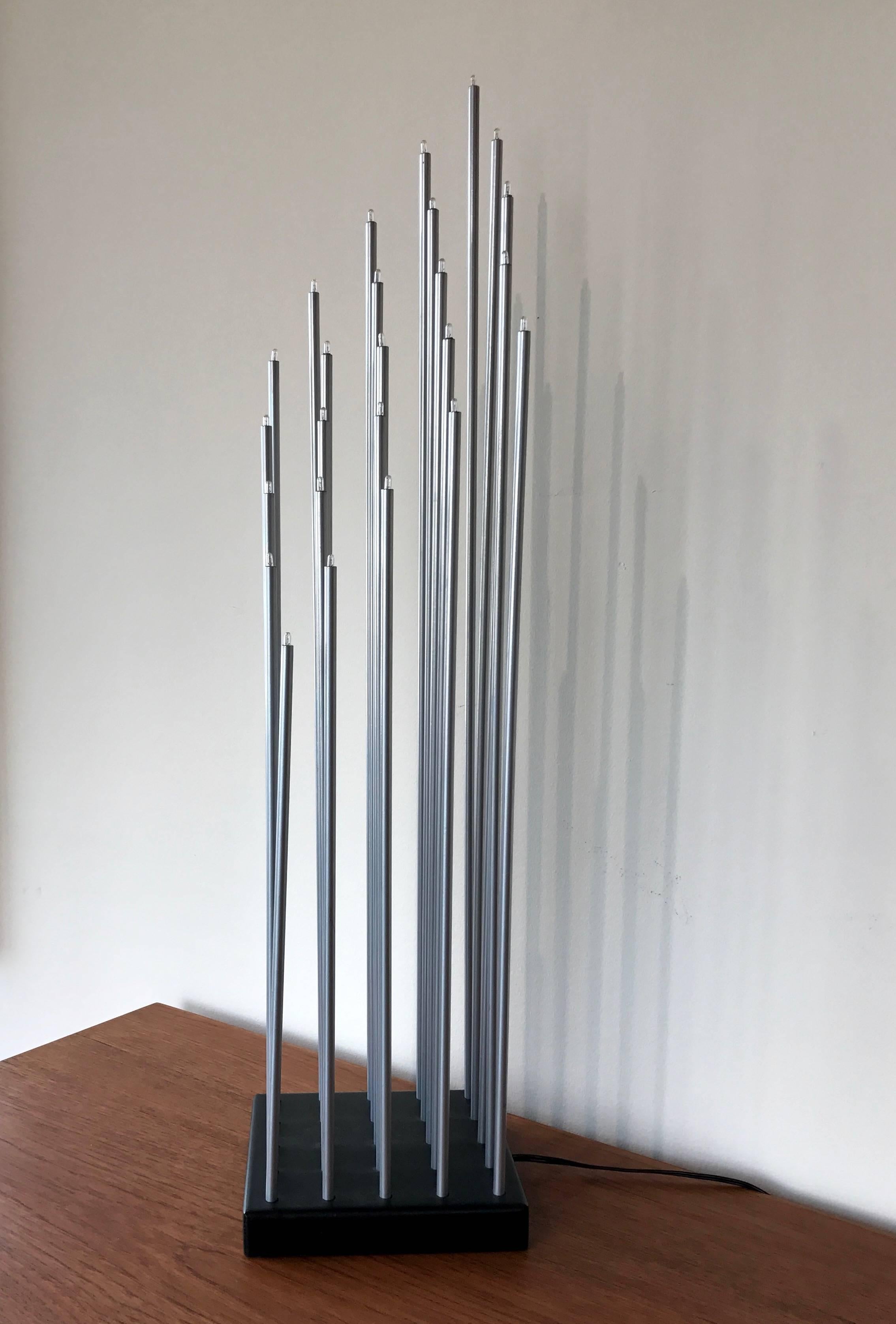 A tall, sculptural and uncommon “Top-Light” Minimalist table lamp comprised of 25 individually illuminated graduated metal rods.

Each aluminum rod is topped by a pill-sized bulb and is equidistantly set in a square wood base finished in satin