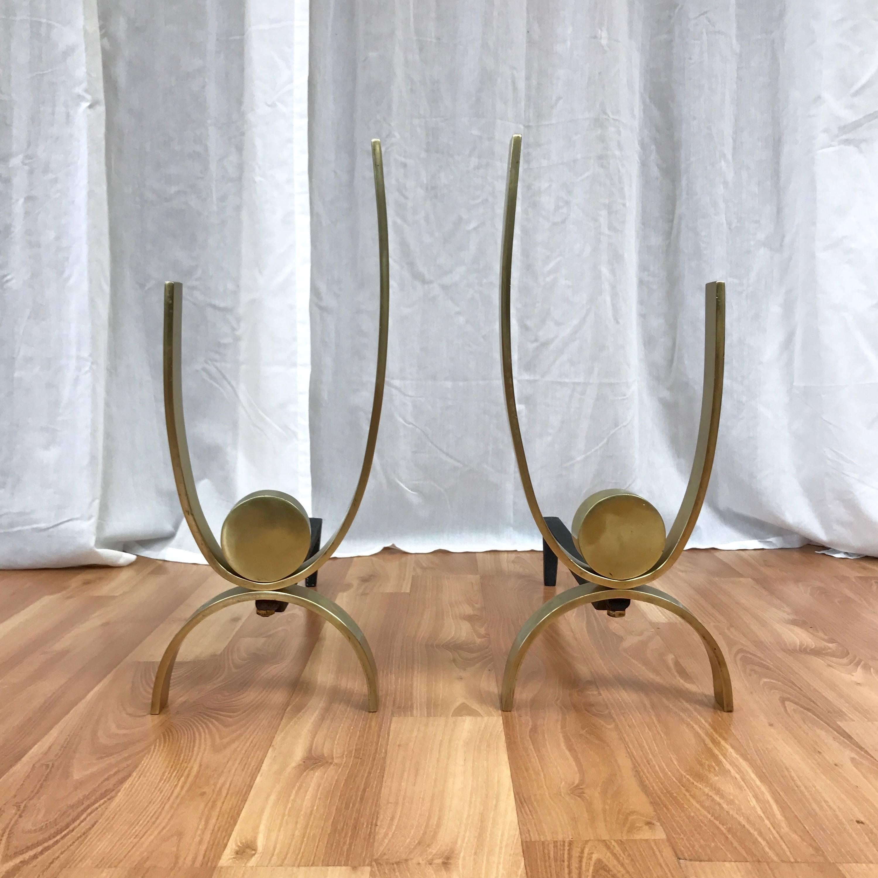A striking pair of tall and substantial brass and iron andirons by important Art Deco and early Mid-Century designer Donald Deskey.

Minimalist design features polished solid brass bands that support and cradle a thick brass puck. Cast iron leg