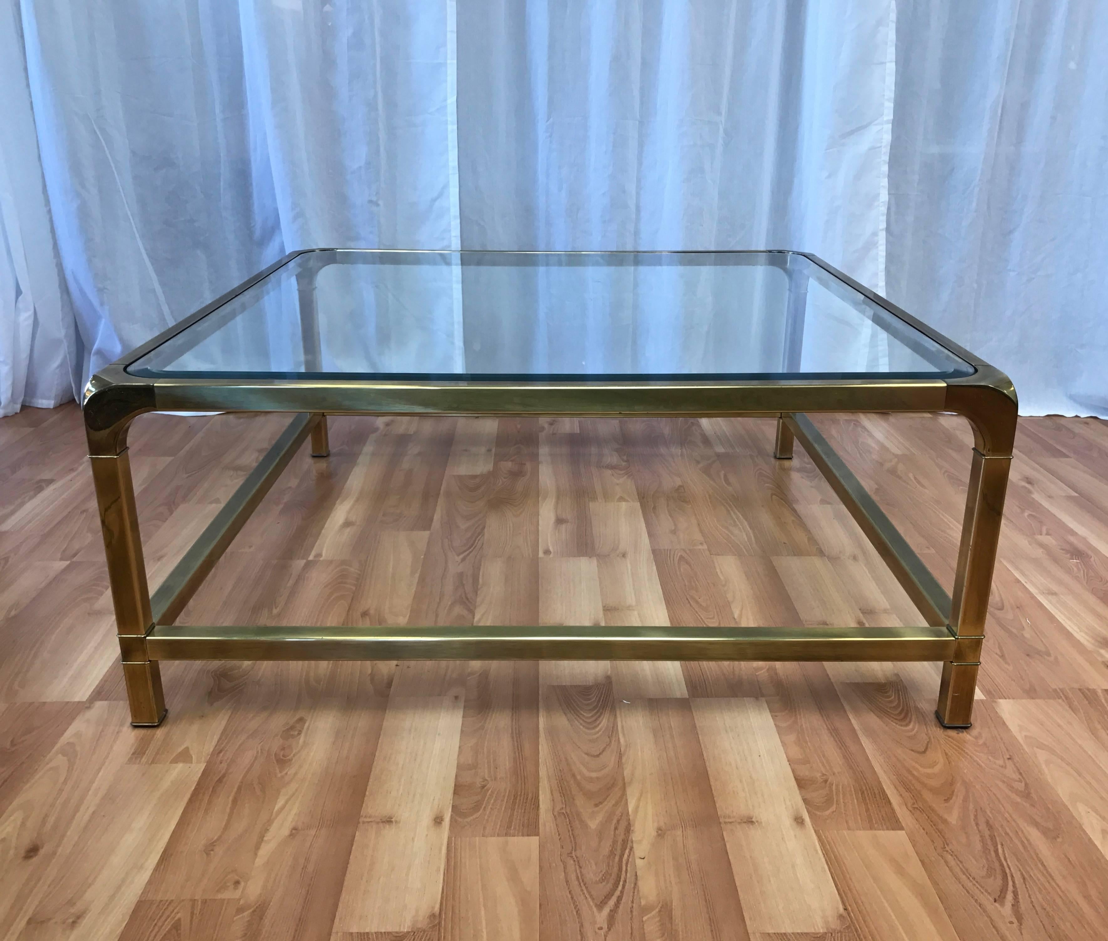 An extremely large square brass and glass coffee or cocktail table by Mastercraft.

Streamlined Hollywood Regency-inspired design displays Mastercraft’s signature waterfall corners, low spanners, and brass with a nicely subdued finish. Has