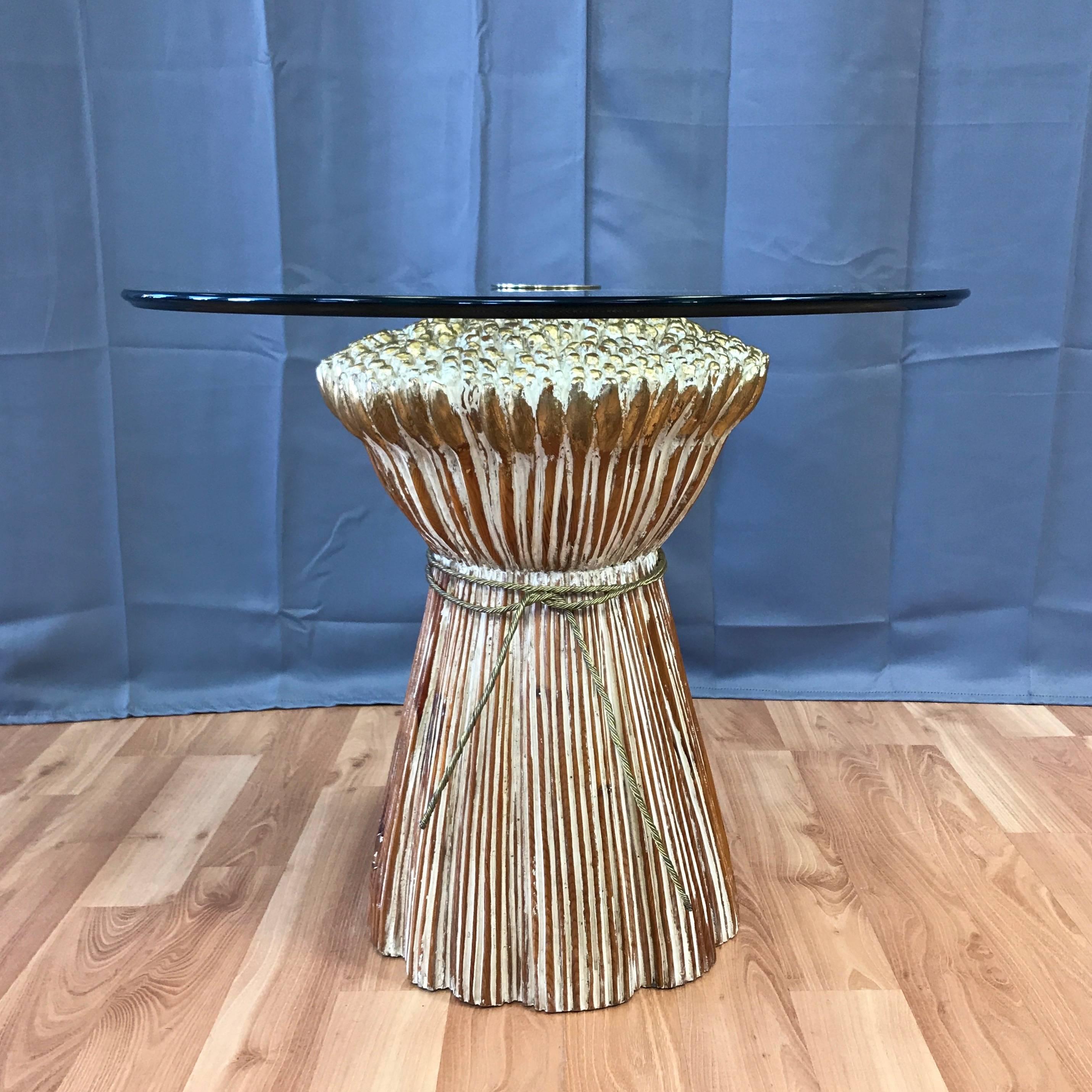 A superb solid wood sheaf of wheat cocktail table with glass top and brass accents.

Beautifully carved base is enhanced by off-white lacquer fills and gleaming gilt accents. A brass finish metal “rope” is tied around its waist. Floating glass top
