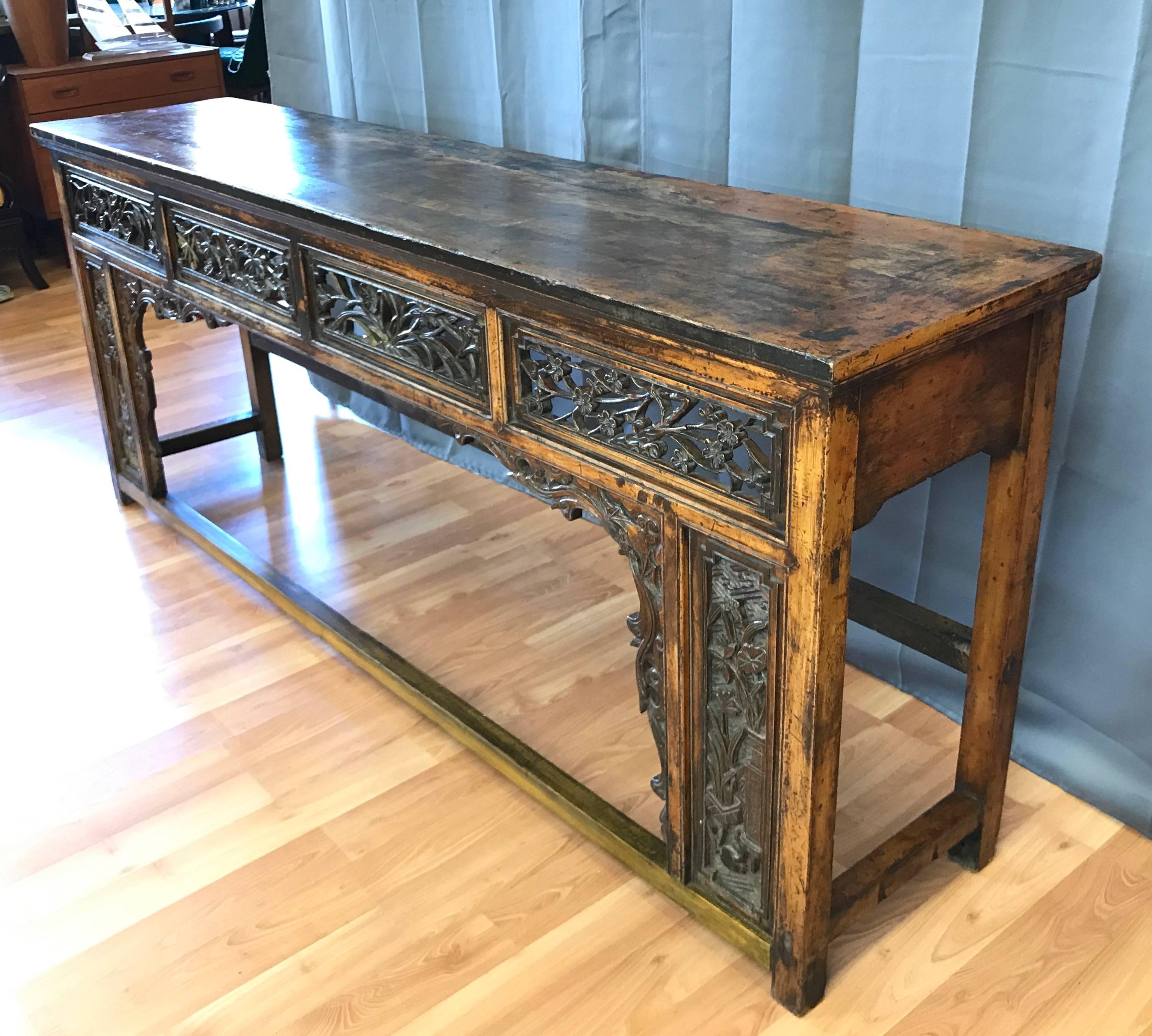 A long antique Chinese altar, console, or sofa table dating from the Qing dynasty.

Delicately hand-carved mahogany apron, deep relief panels, and intricate skirt embellishments have a lively flora motif that invites closer inspection. Table is
