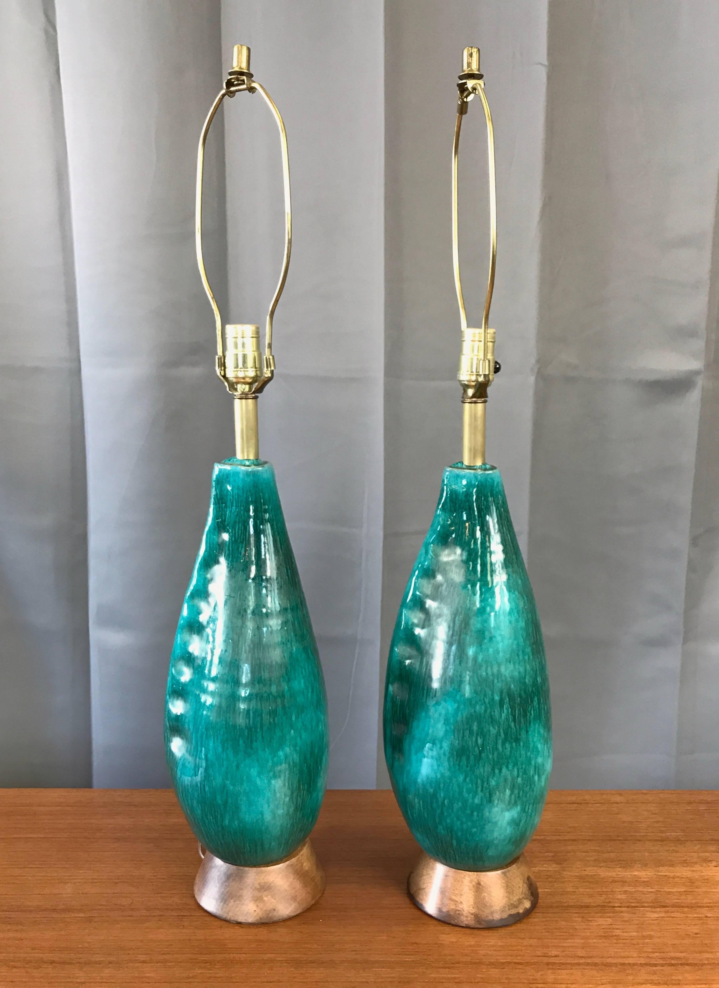 A pair of Mid-Century turquoise ceramic table lamps with wood bases by Marcello Fantoni.

Design slyly references its Italian roots with a calzone-like body and finger-pinched edge. Multi-layered glaze has a very vibrant turquoise ground washed in