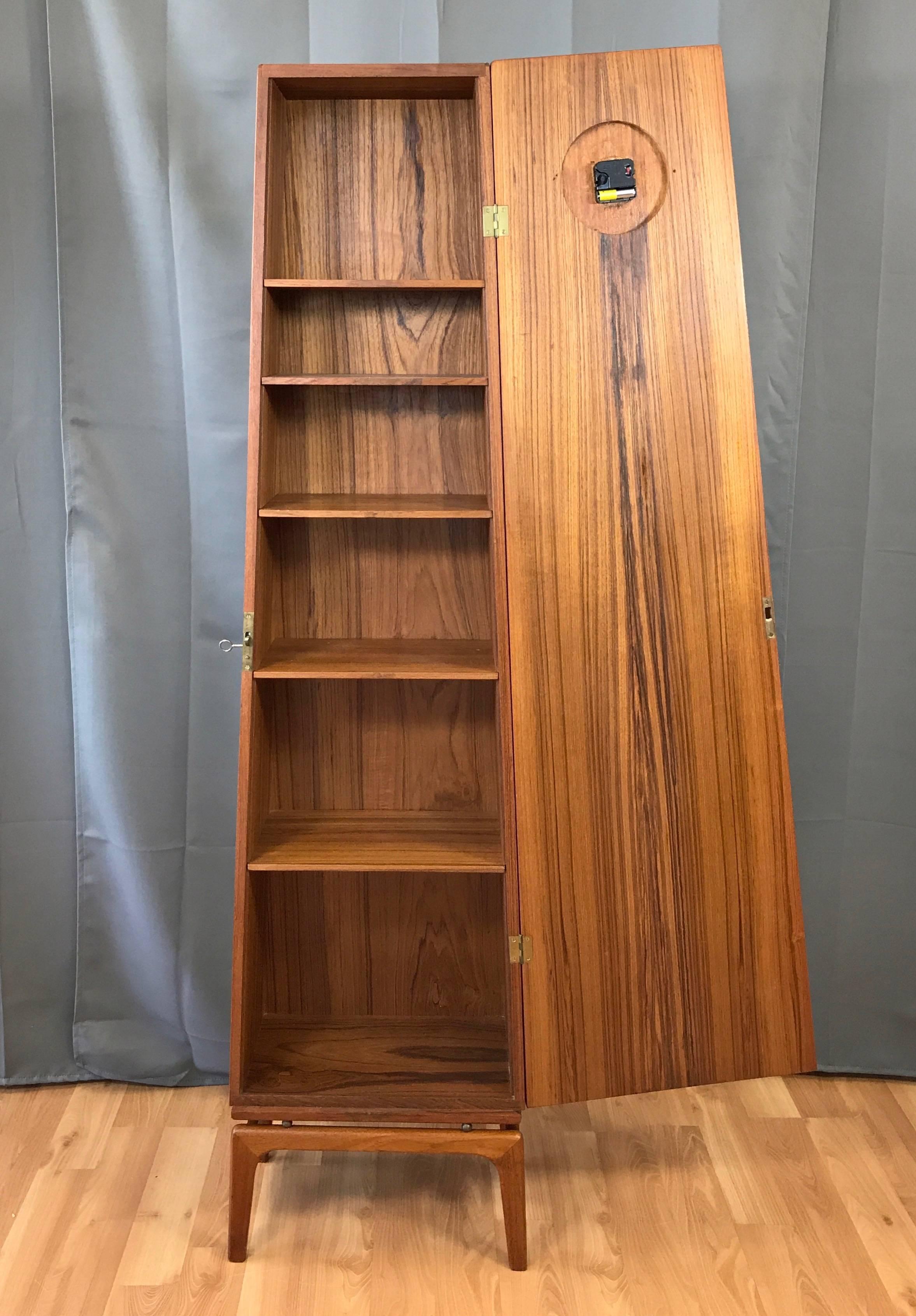 A Mid-Century Modern Danish teak grandfather clock with locking cabinet. 

Obelisk-shaped cabinet is finished inside and out in nicely figured bookmatched teak veneer. Brass ball spacers give it the appearance of floating above a sculptural solid