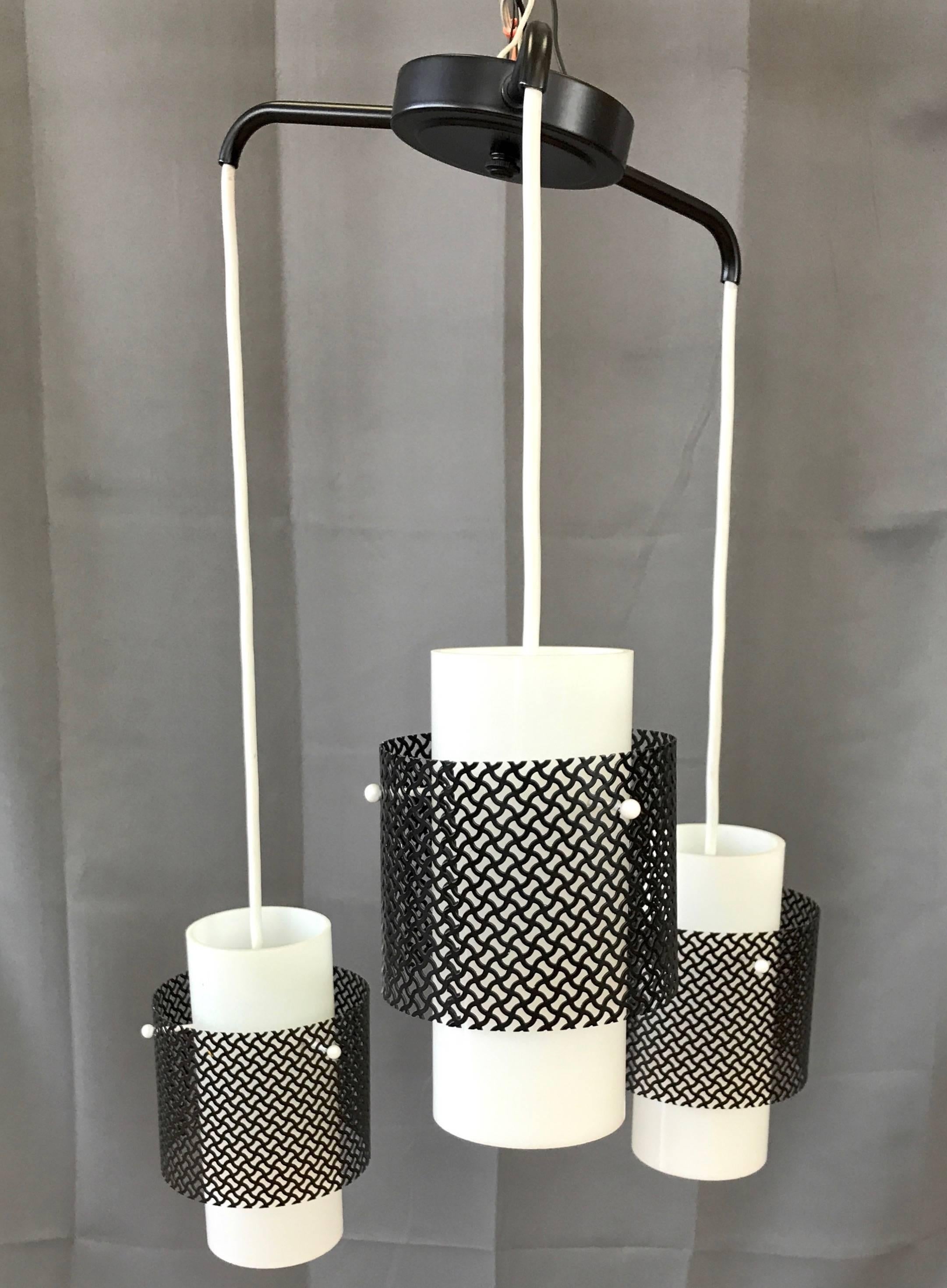 A sharp looking Mid-Century Modern three-light ceiling fixture with glass shades and metal diffusers.

Milk white cylindrical glass shades hang in a staggered arrangement from outstretched black enameled metal arms. Each shade is pierced and