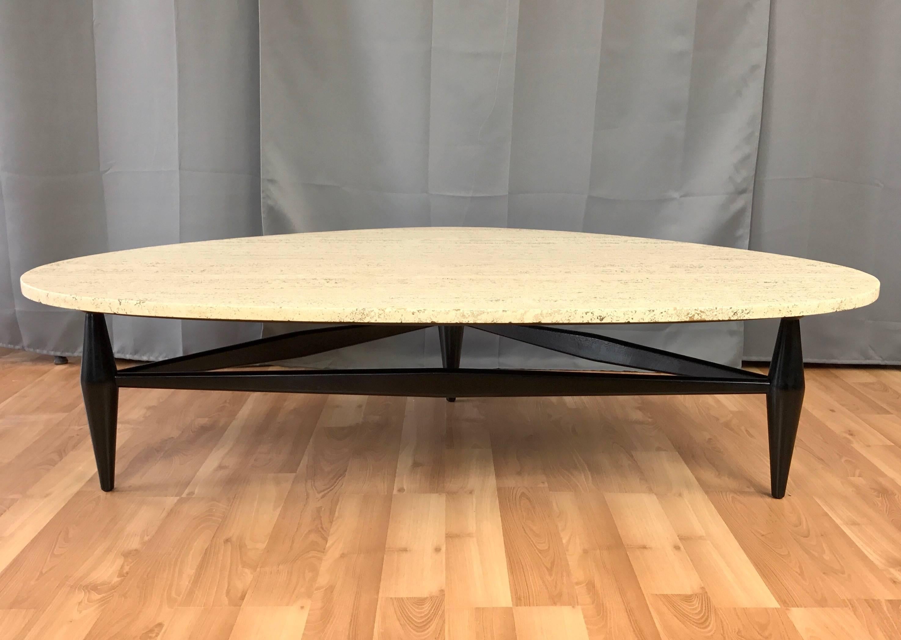 A very handsome Mid-Century travertine coffee table with a sculptural three-point black lacquered wood base.

Generously sized top is a three-sided ovoid slab of satin finish 3/4“ travertine with a very active and attractive pattern. It sits on a