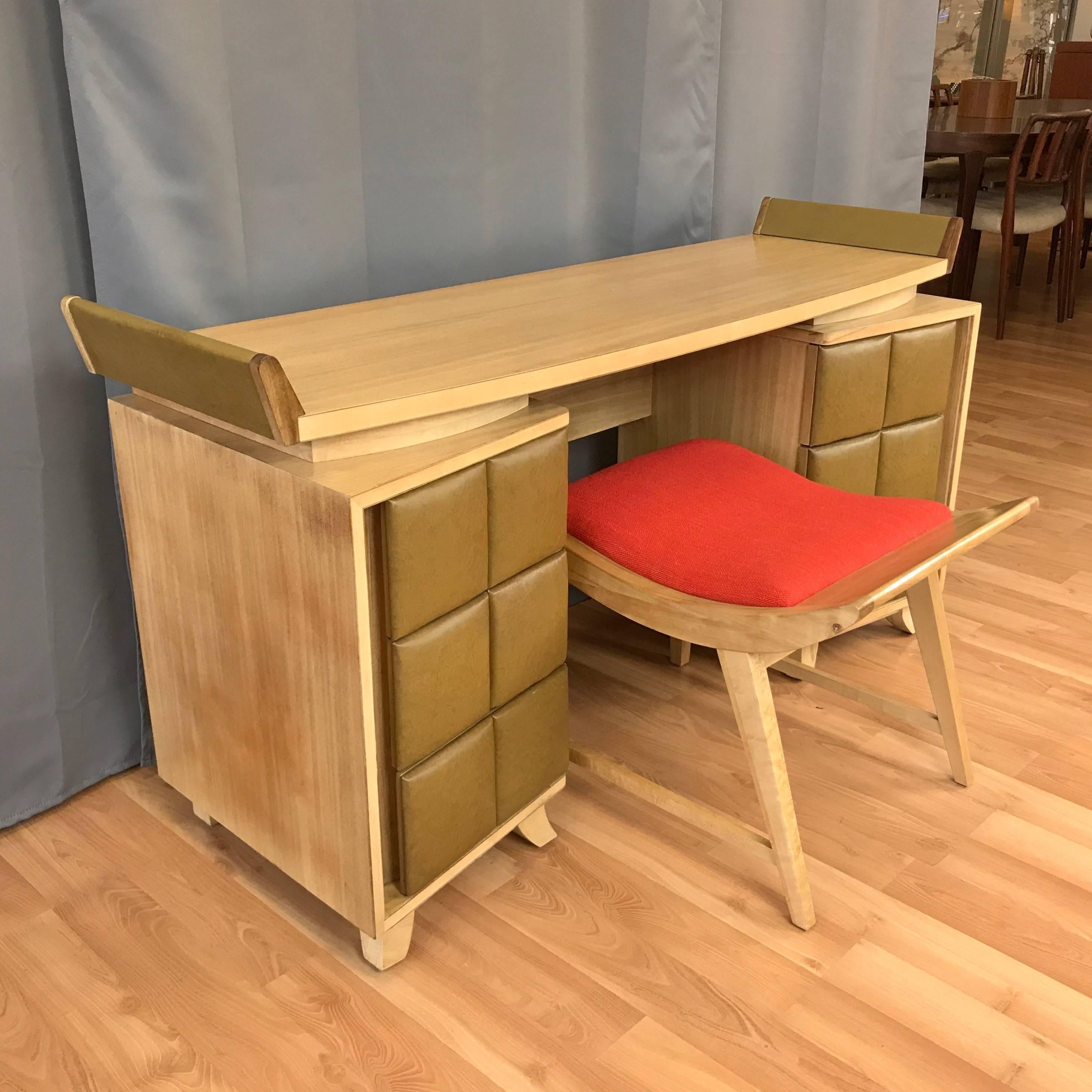 An early mid-century vanity and bench set by master of American modernism Gilbert Rohde for Herman Miller.

Vanity or writer’s desk in birch and quartered birch veneer. Top has slightly curved front edge and floats above a pair of angled cabinets,