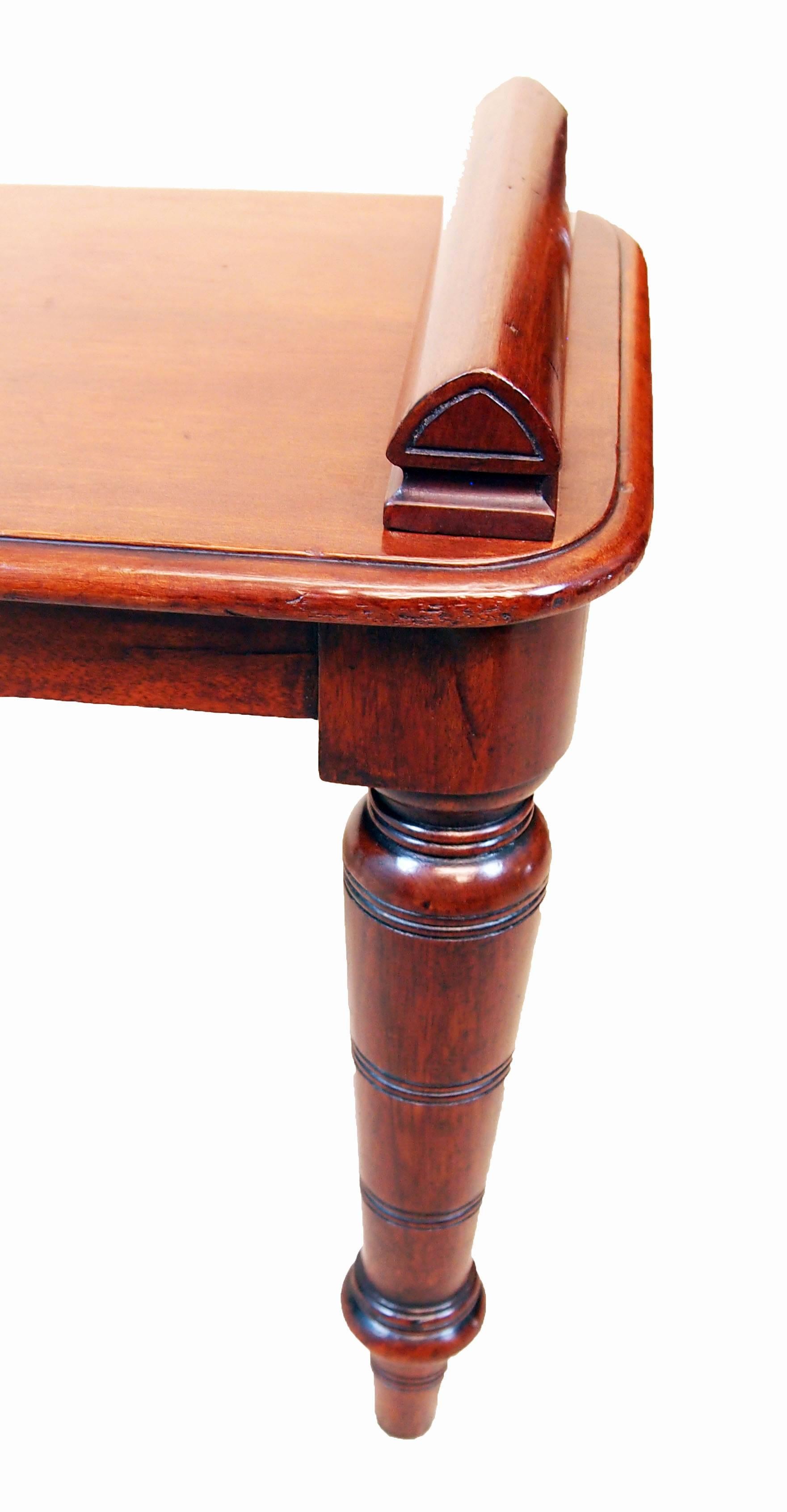 A late 19th century mahogany hall bench, or window seat, of diminutive
Proportion having triangulated rolls to ends of rectangular top raised
On four ring turned tapering legs.