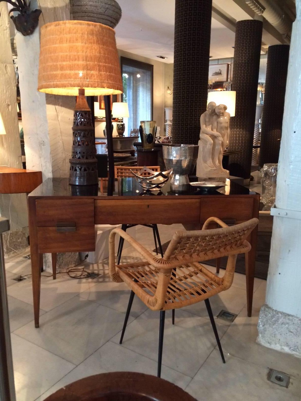 A chocolate-colored and perforated ceramic table lamp with a straw shade.