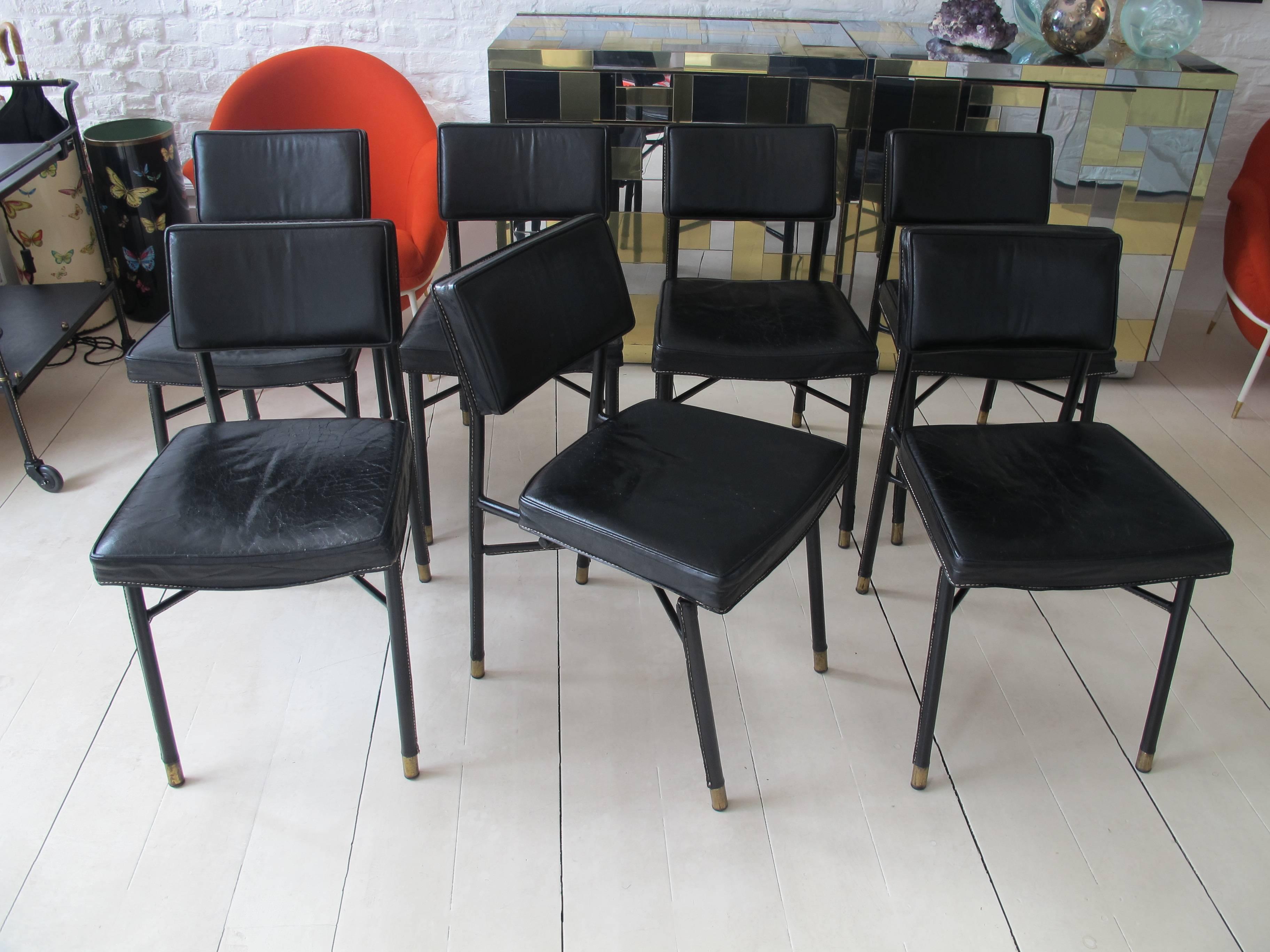 Set of seven stitched leather dining chairs, brass feet designed by by Jacques Adnet, circa 1950, France.
