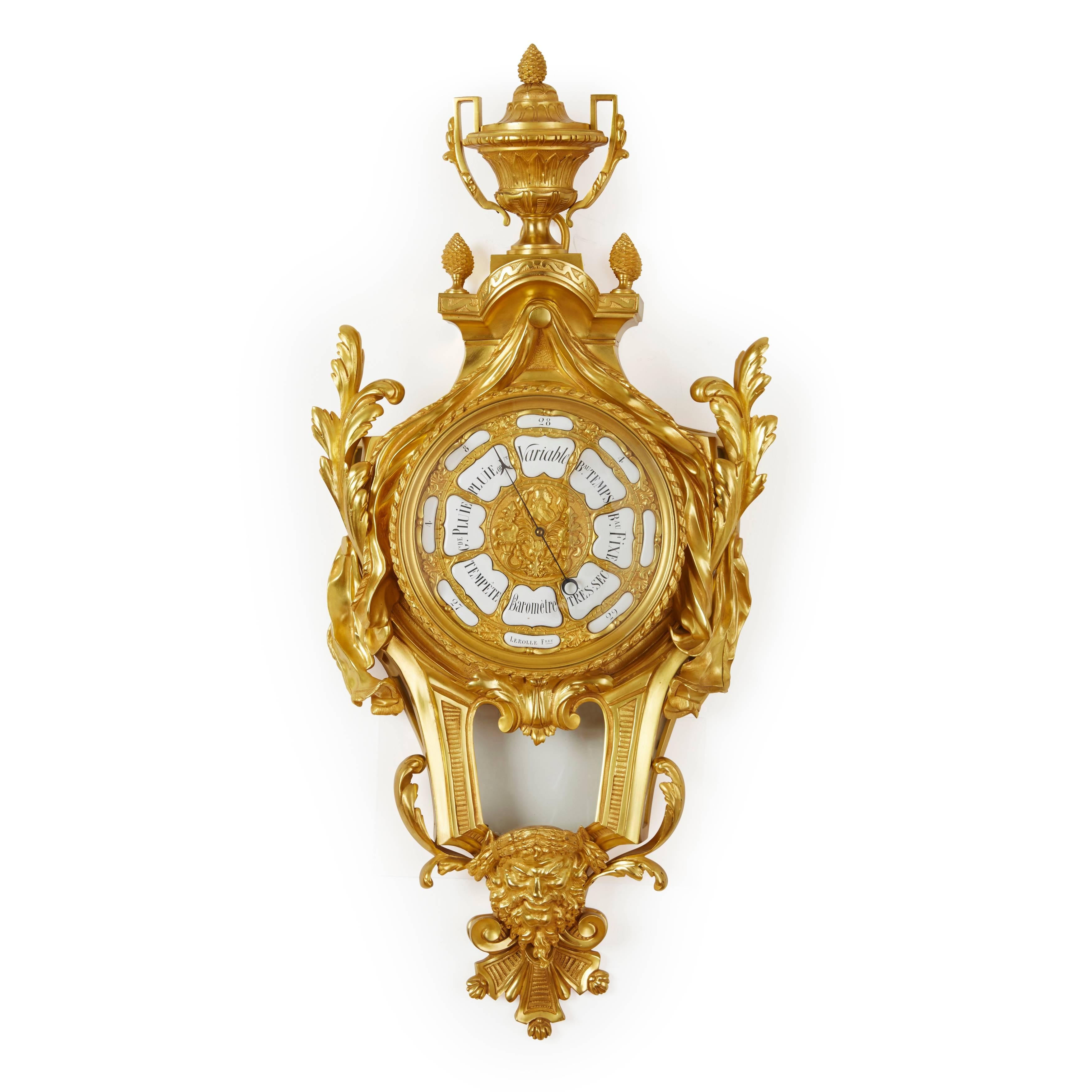 The clock and barometer constructed in gilded bronze and featuring enamel plaques to the dial; each decorated with classical motifs included scrolling acanthus leaves and pine cone finials and surmounted with lidded urns and featuring satyr heads at