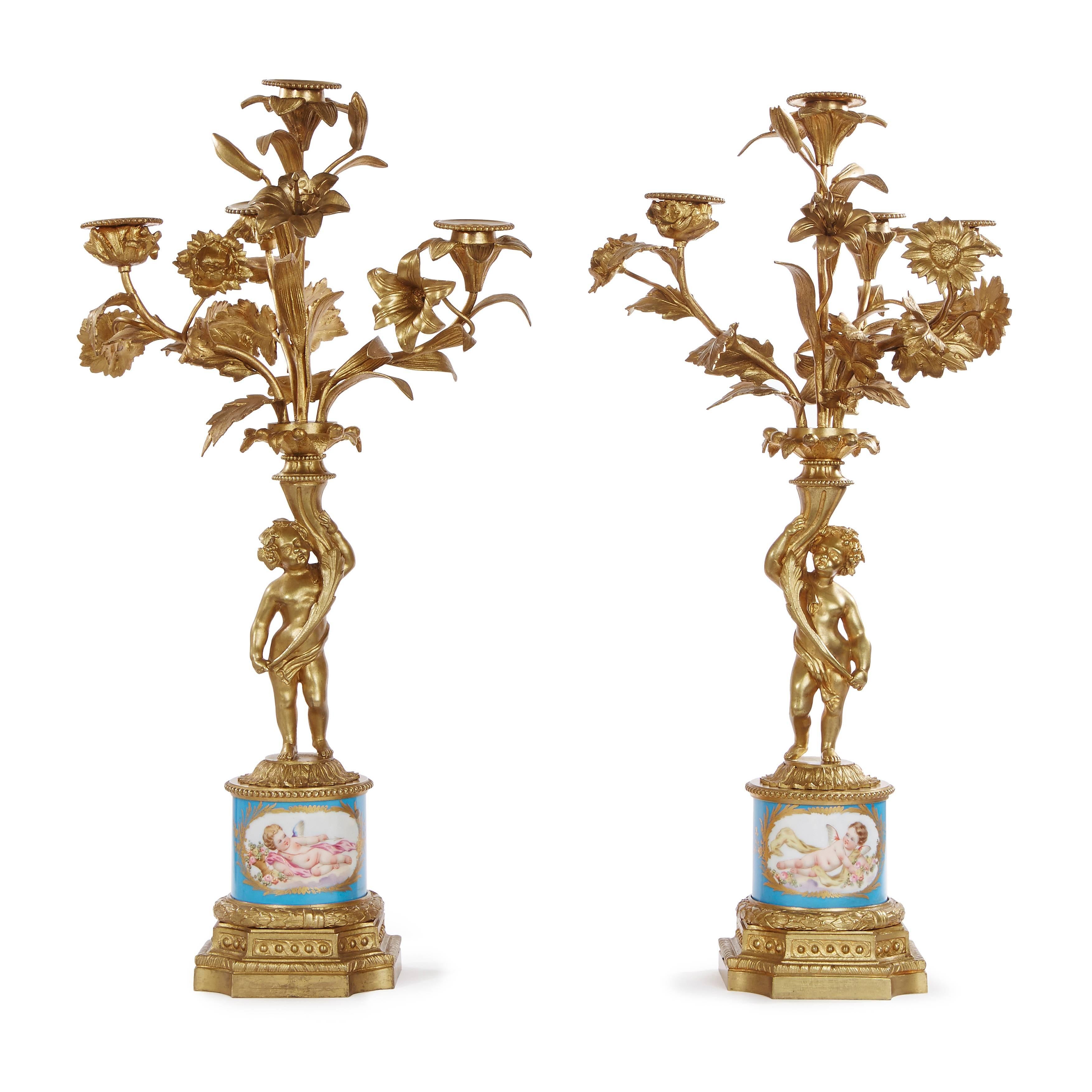 Comprising a central clock and a pair of flanking candelabra, the clock with central circular dial signed 'PICARD / A GENEVE', surrounded by three ormolu cherubs and two porcelain plaques depicting flowers and cherubs, all housed within an ormolu