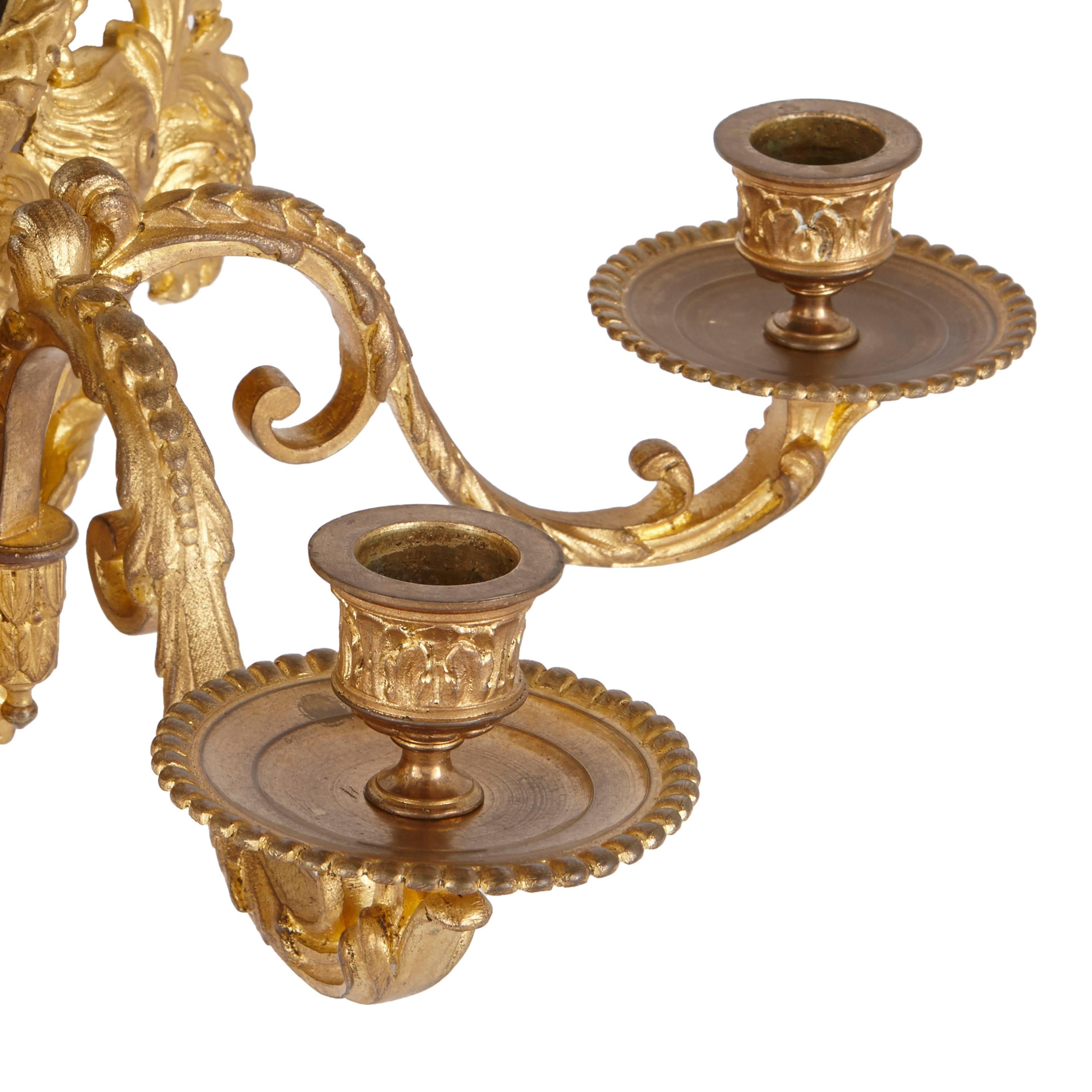 Two ormolu wall lights decorated in the ornate and florid Rococo style, each featuring central circular mirrors and two lighting branches.