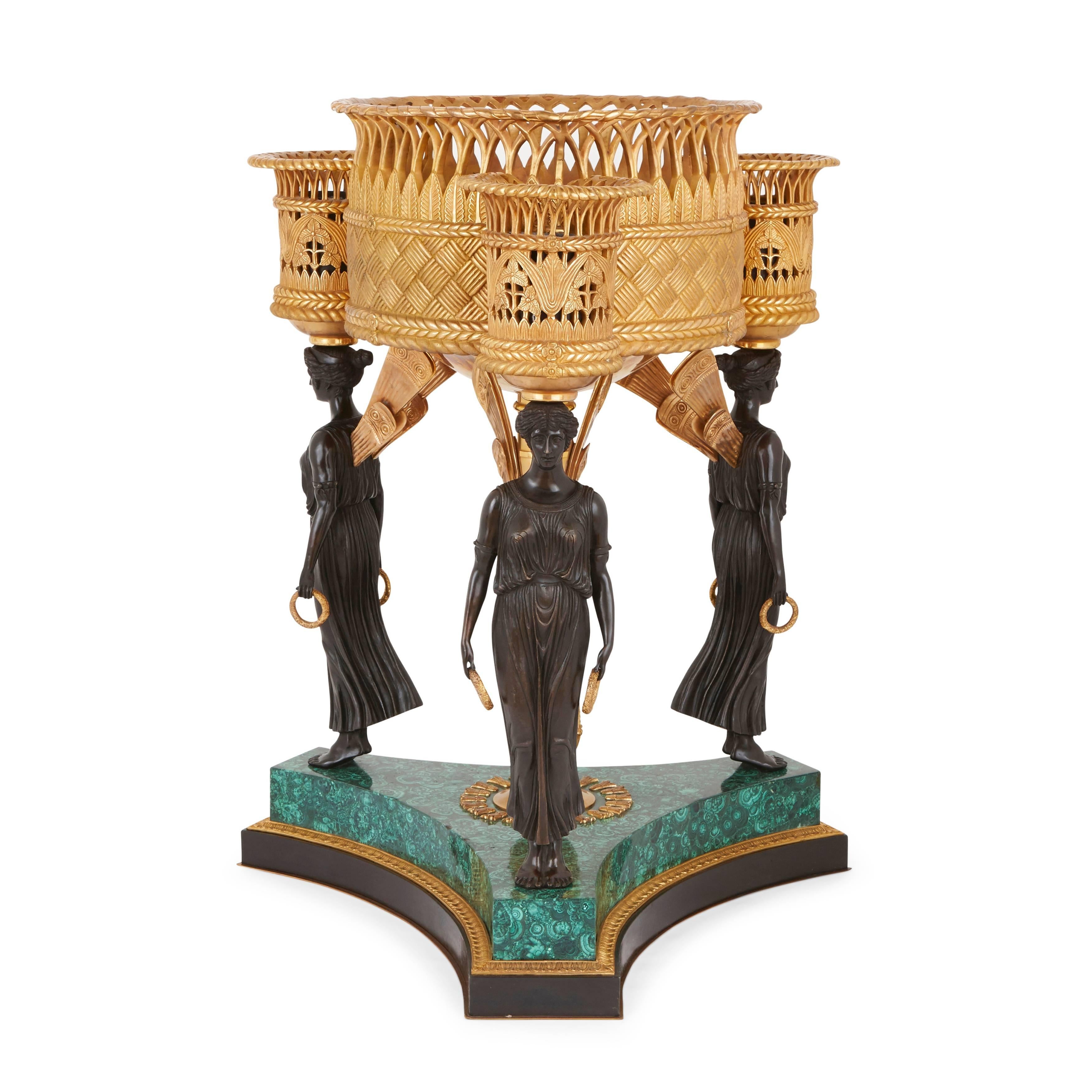 Each with central circular ormolu jardiniere with an openwork pierced basket gallery top and three smaller ones to each corner, above three patinated bronze caryatid standing figures with gilt wings, on a shaped malachite and bronze base centred