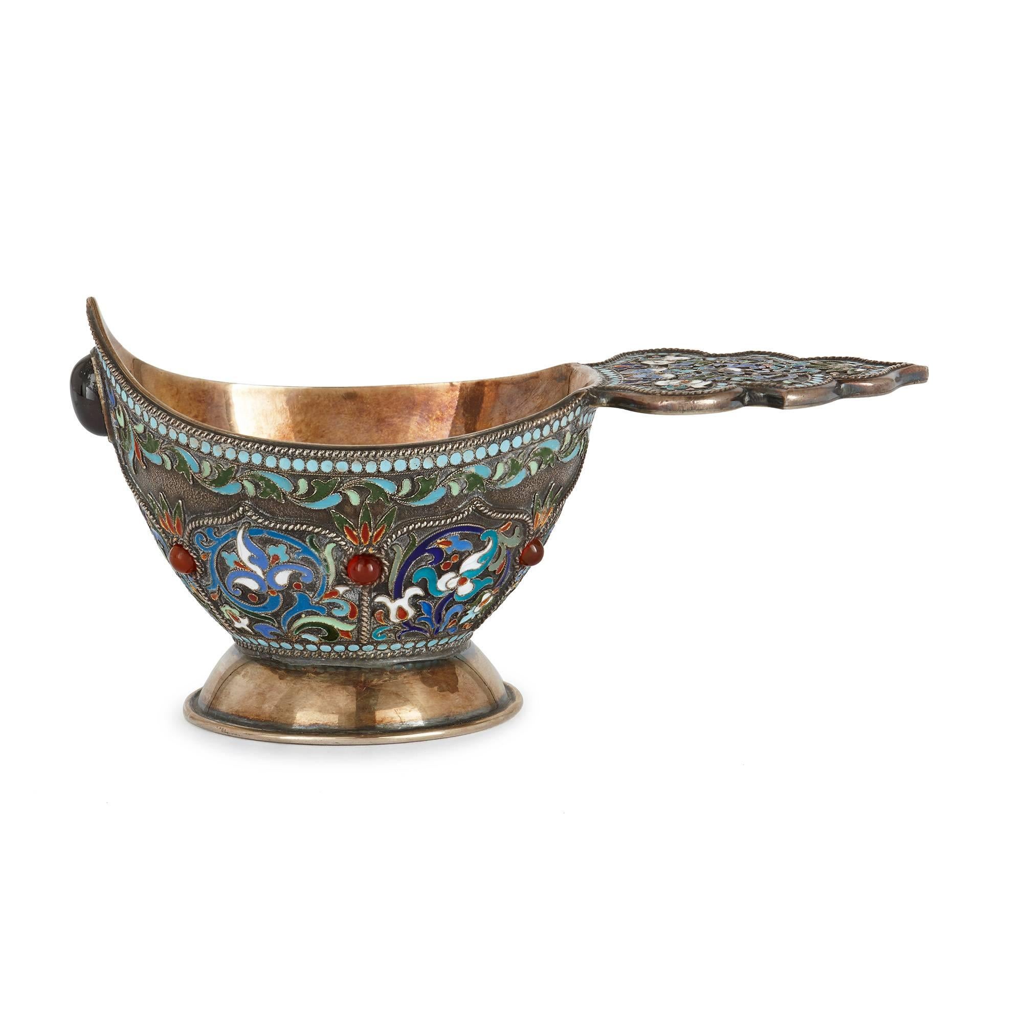 The silver gilt kovsch decorated in cloisonné enamel with a pattern of leaves and flowers, set with polished gemstones, marks to the underside.

The kovsch is a traditional Russian drinking vessel, featuring a boat shaped bowl and handle, that