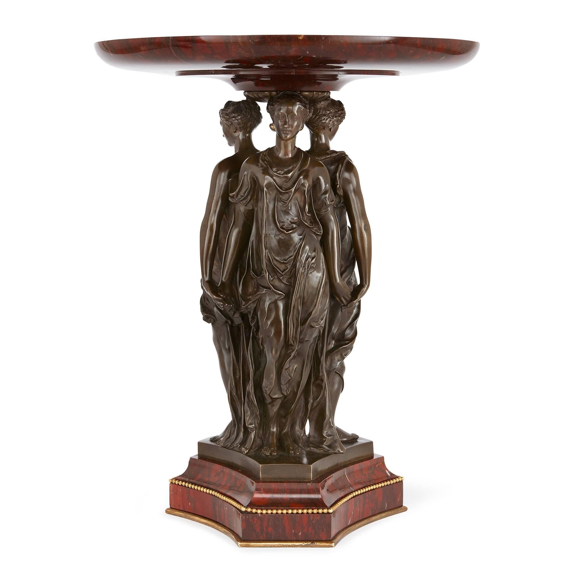 In an ornamental style, with rouge griotte marble and burnished bronze depicting the three Graces, signed 'A. ROBBE. Paris.'

This stunning French centrepiece depicts the three Graces, the beautiful sister goddesses from Greek mythology, tenderly