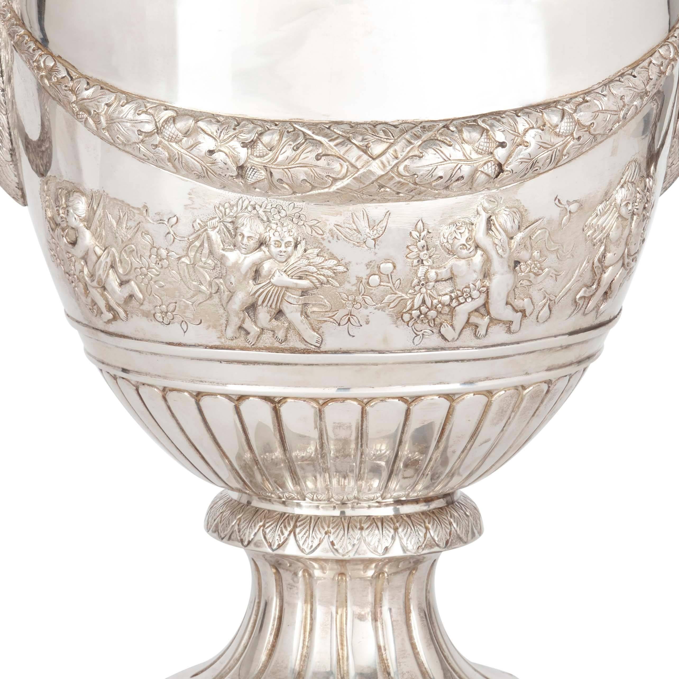 Each with twin handles as ram's heads, decorated with dancing putti, flowers, garlands of flowers and acanthus leaves, with marks to base.

These splendid silver vases would make a sophisticated addition to any interior, imparting a touch of