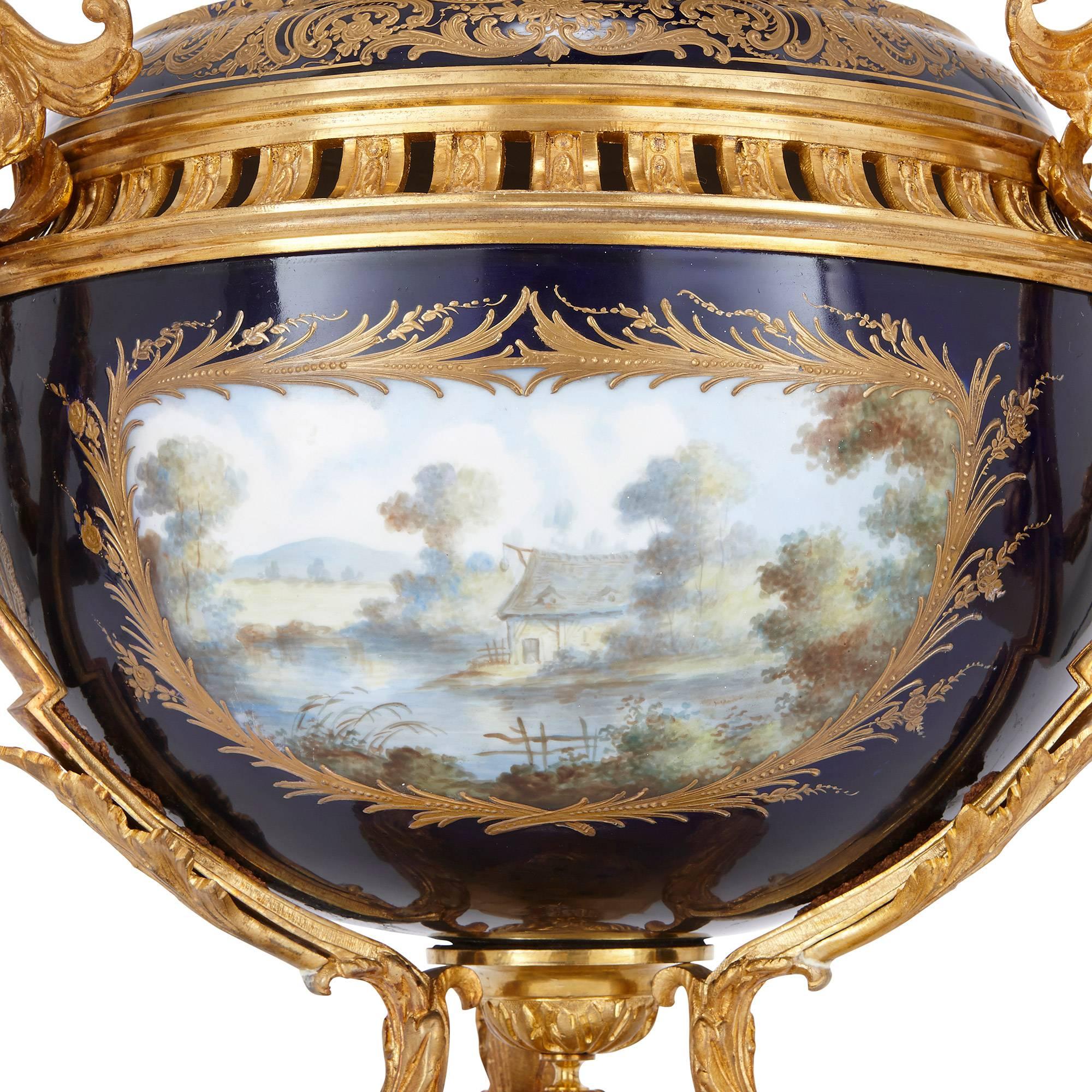 The dark blue ground body painted to the front with playful and amorous pastoral scenes, decorated throughout with gilt rocaille motif, mounted with twin ormolu handles shaped as winged classical female busts, surmounted by a shaped bulbous cover