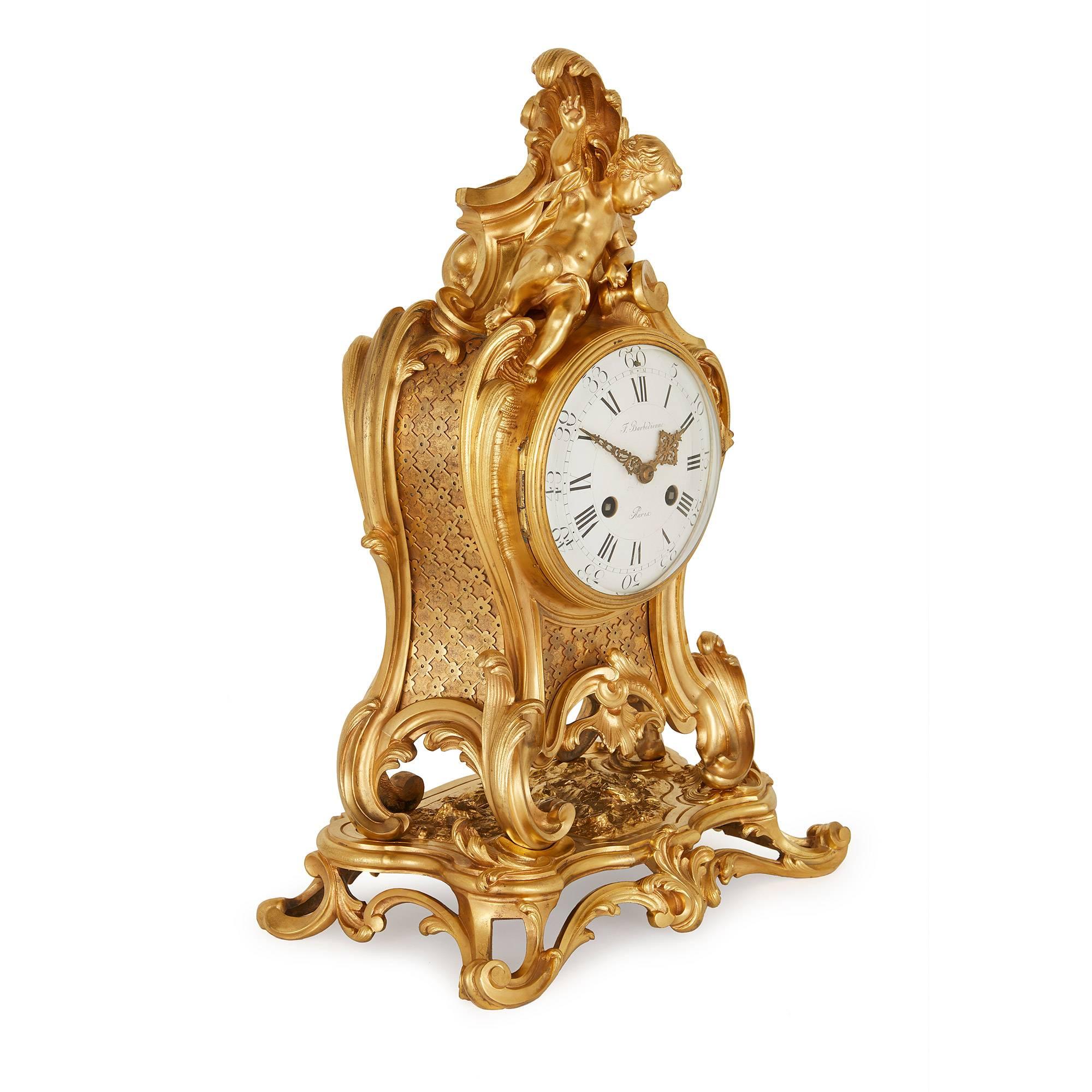 Comprising a central clock and a pair of flanking candelabra, the ormolu clock with circular dial and roman numbers signed 'F. Barbedienne', decorated with foliate scrolls and shells, surmounted by a putto, the pair of flanking three light