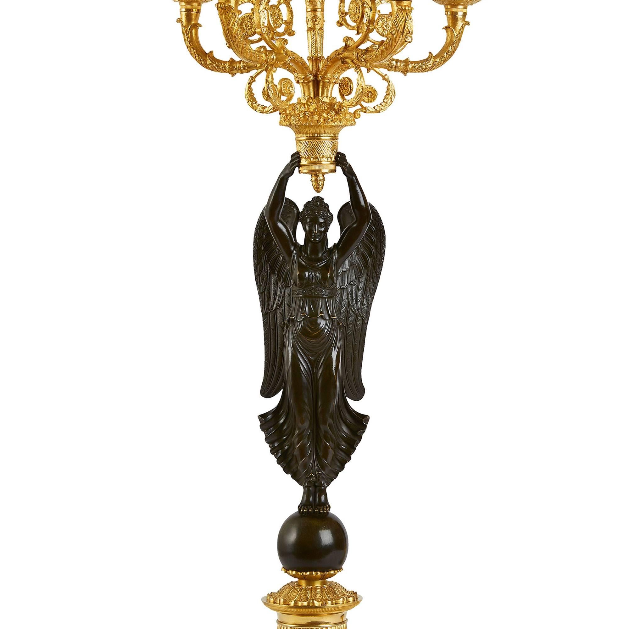 Each with winged figures of Victory holding aloft multi candelabra with scrolled branches each terminating in drip pans and nozzles, whilst standing on spheres.

These impressive candelabra with winged figures of Victory derive from a design for