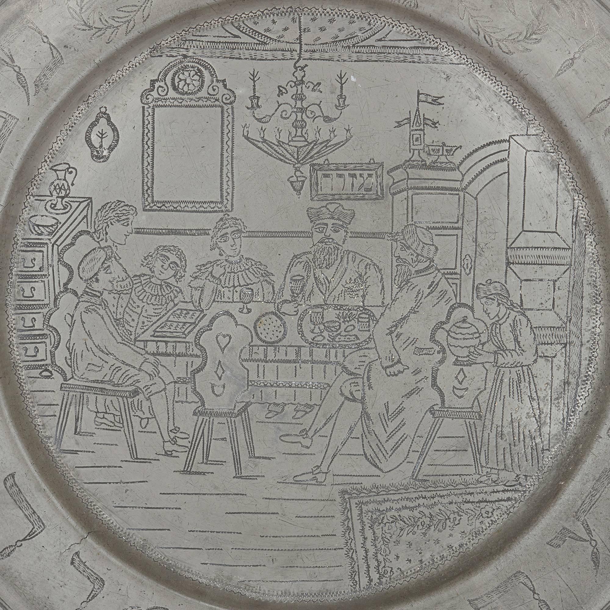The fine German antique pewter plate depicts a family scene, as the group sits at the table during the Passover Seder. Around the rim of the plate are various engraved Hebrew inscriptions, and a Star of David that sits at the top of the plate's