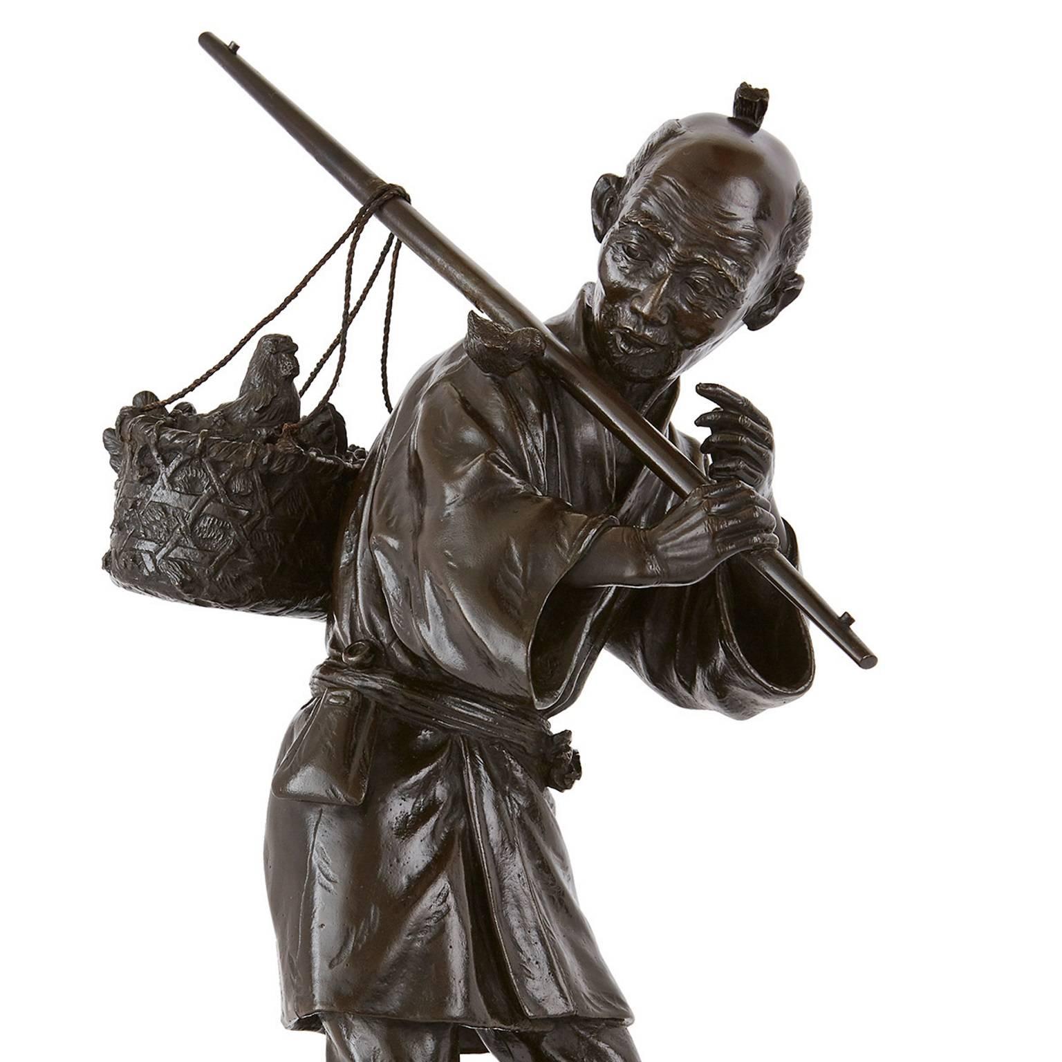 This unique Japanese bronze sculpture depicts an elderly man dressed in the traditional clothing of a Japanese peasant. The old man holds a rod that carries a basket balanced over it, and stands on a base that is signed to the edge. The sculpture