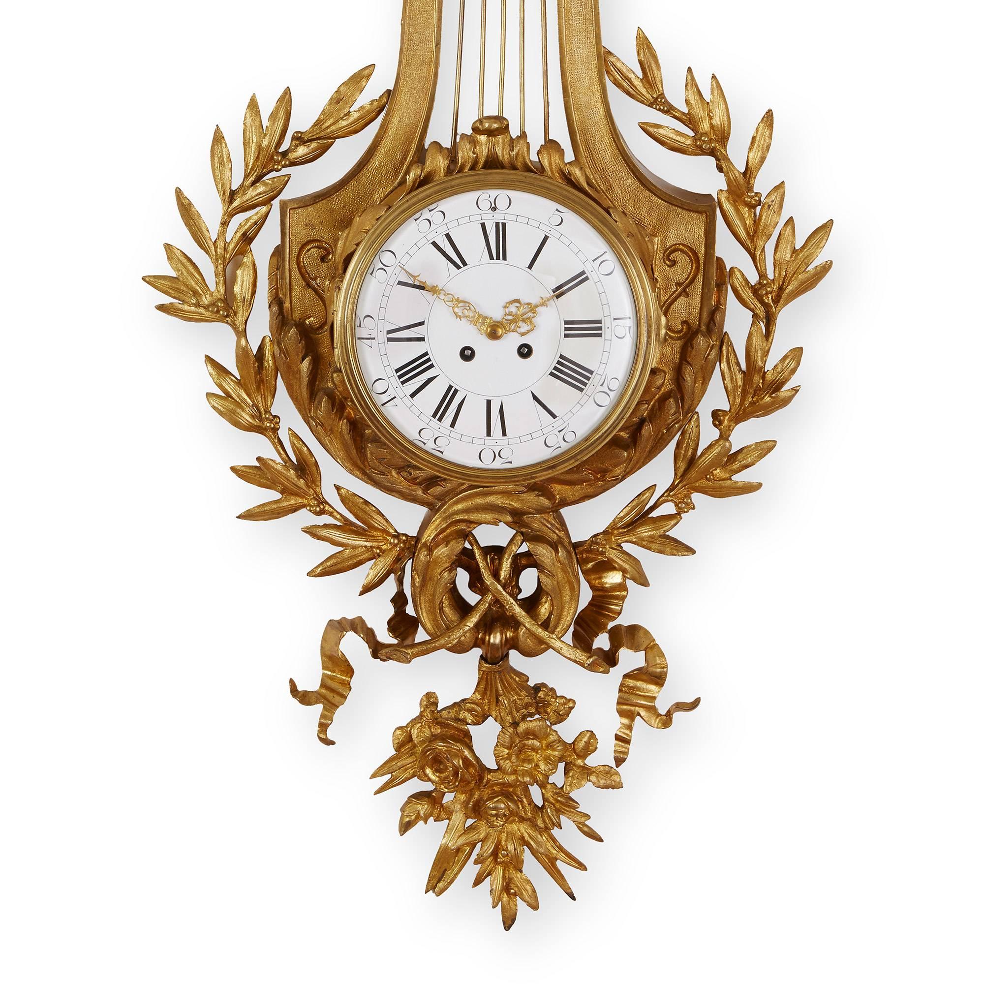 This elegant Cartel clock is decorated the refined neoclassical style. The wall clock features an unusual lyre shaped back plate and a double headed eagle surmount crowned by an ornate bow. The dial has both Roman and Arabic numerals and is