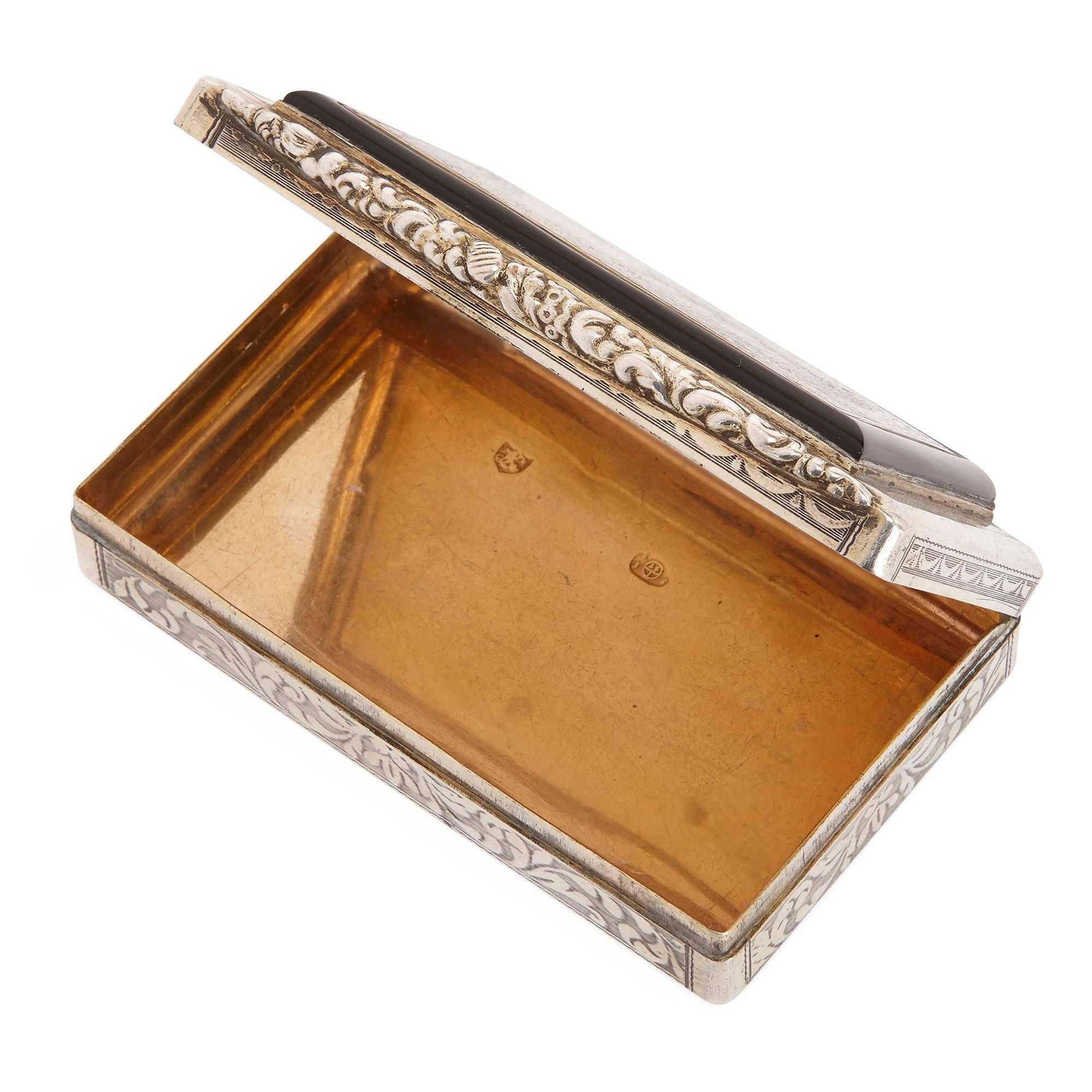 The small rectangular silver snuff box, chased with foliage decorations and featuring a hinged back, is set with a detailed micromosaic plaque on top. The plaque depicts a rural landscape with Roman ruins and two figures standing in front of the